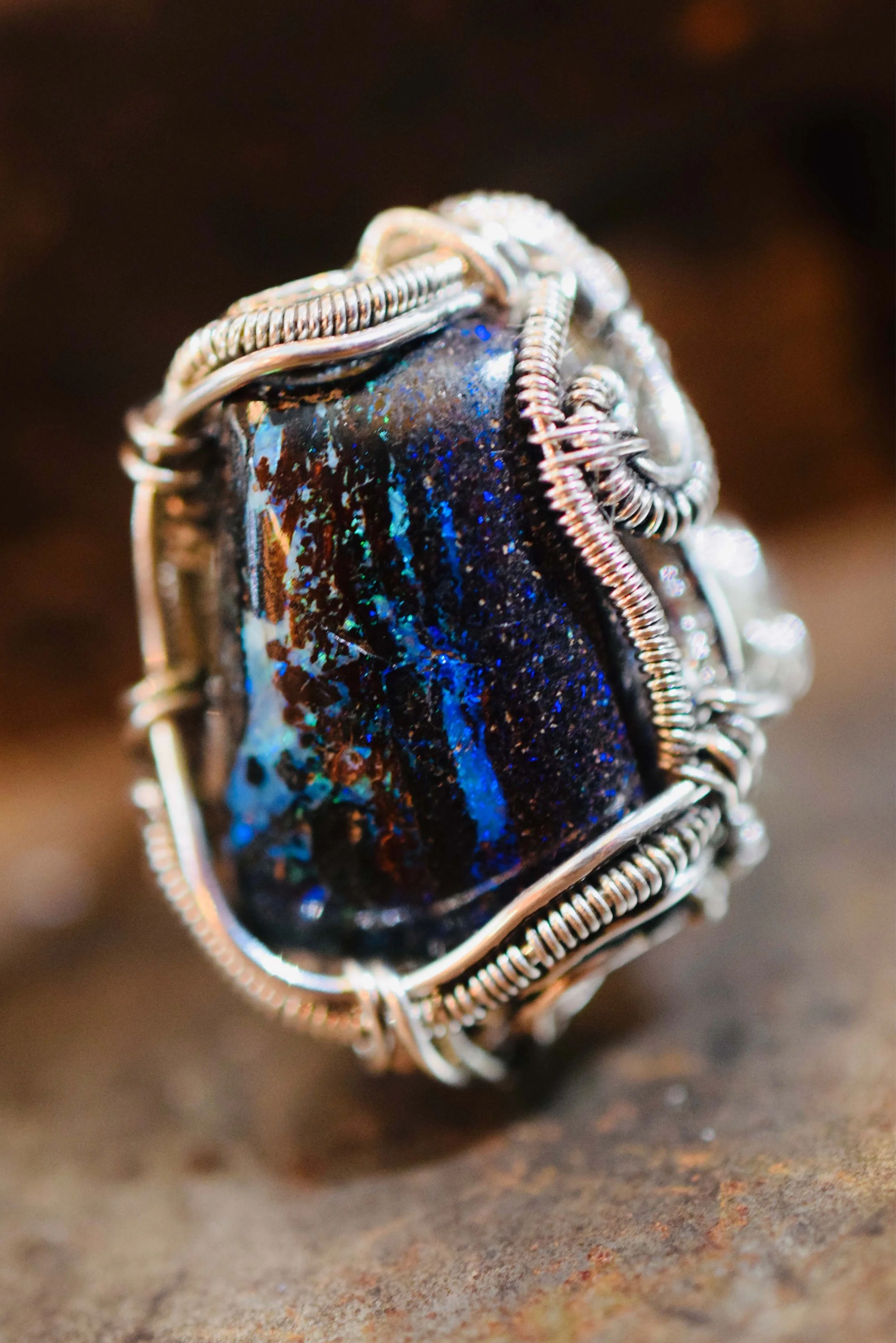 Close-up of a wire-wrapped ring featuring a large, oval-shaped iridescent stone with black, blue, and green hues.