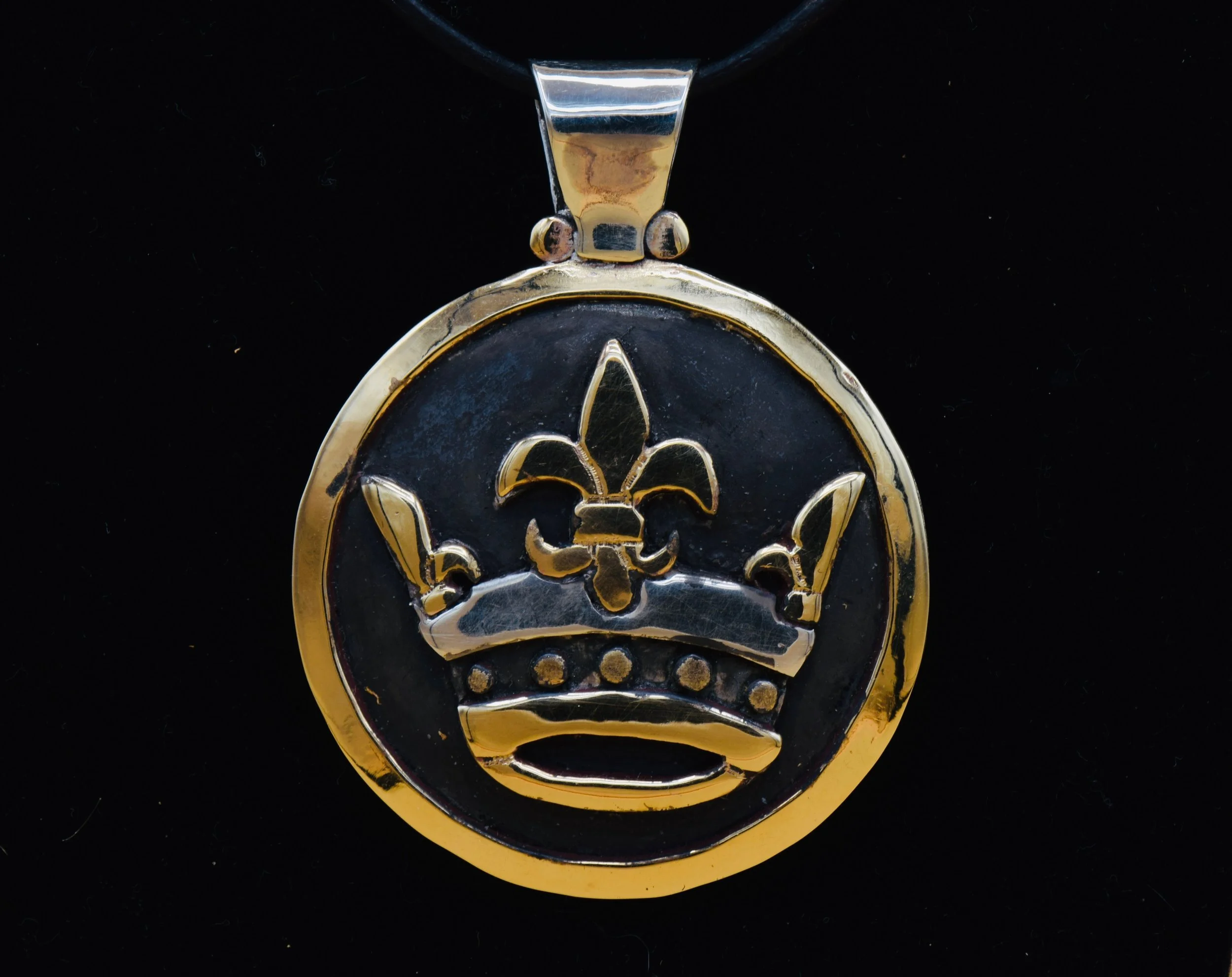 Gold pendant with a black background featuring a crown and fleur-de-lis symbols.