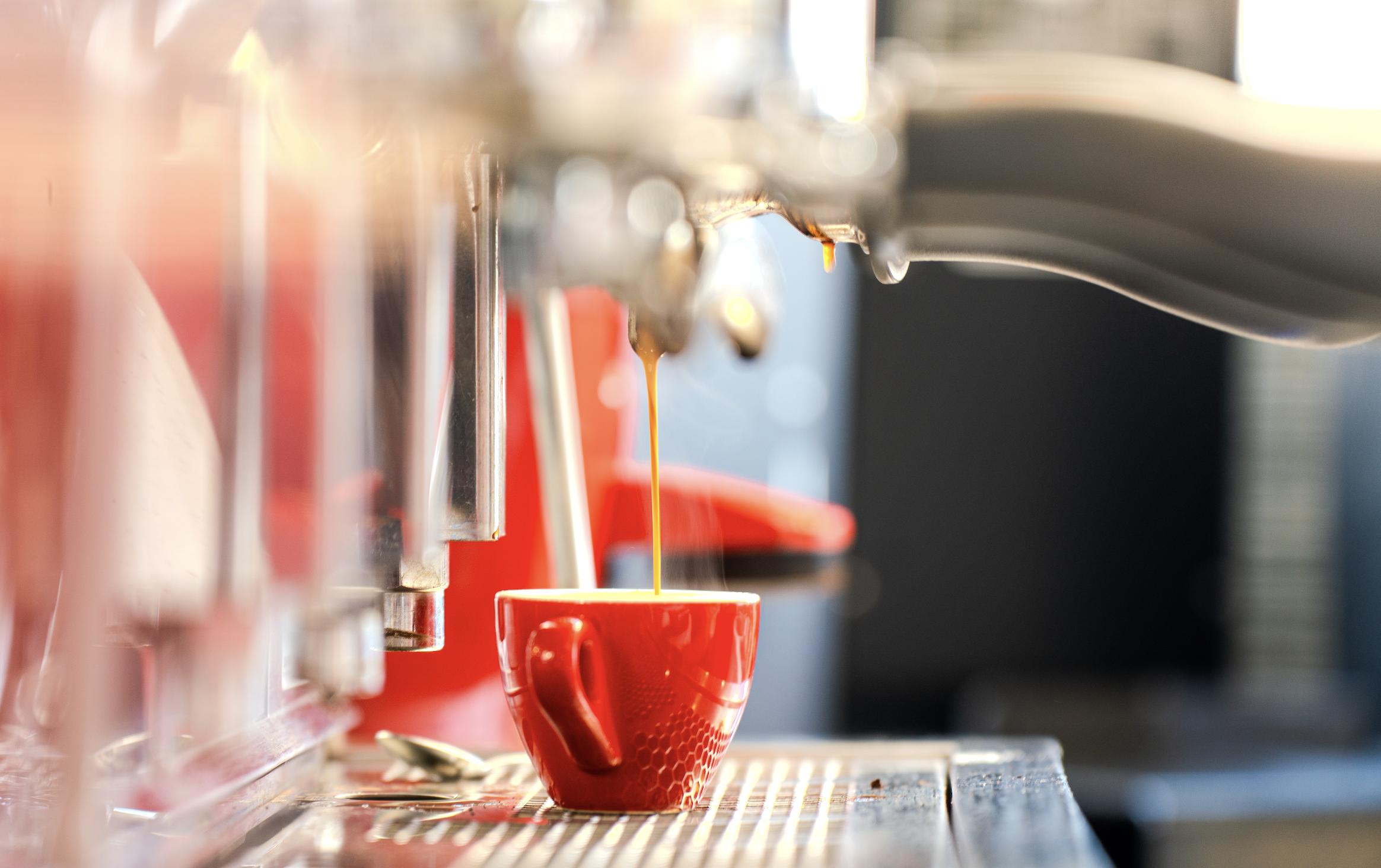 Close-up of an espresso machine pouring dark coffee into a red cup.