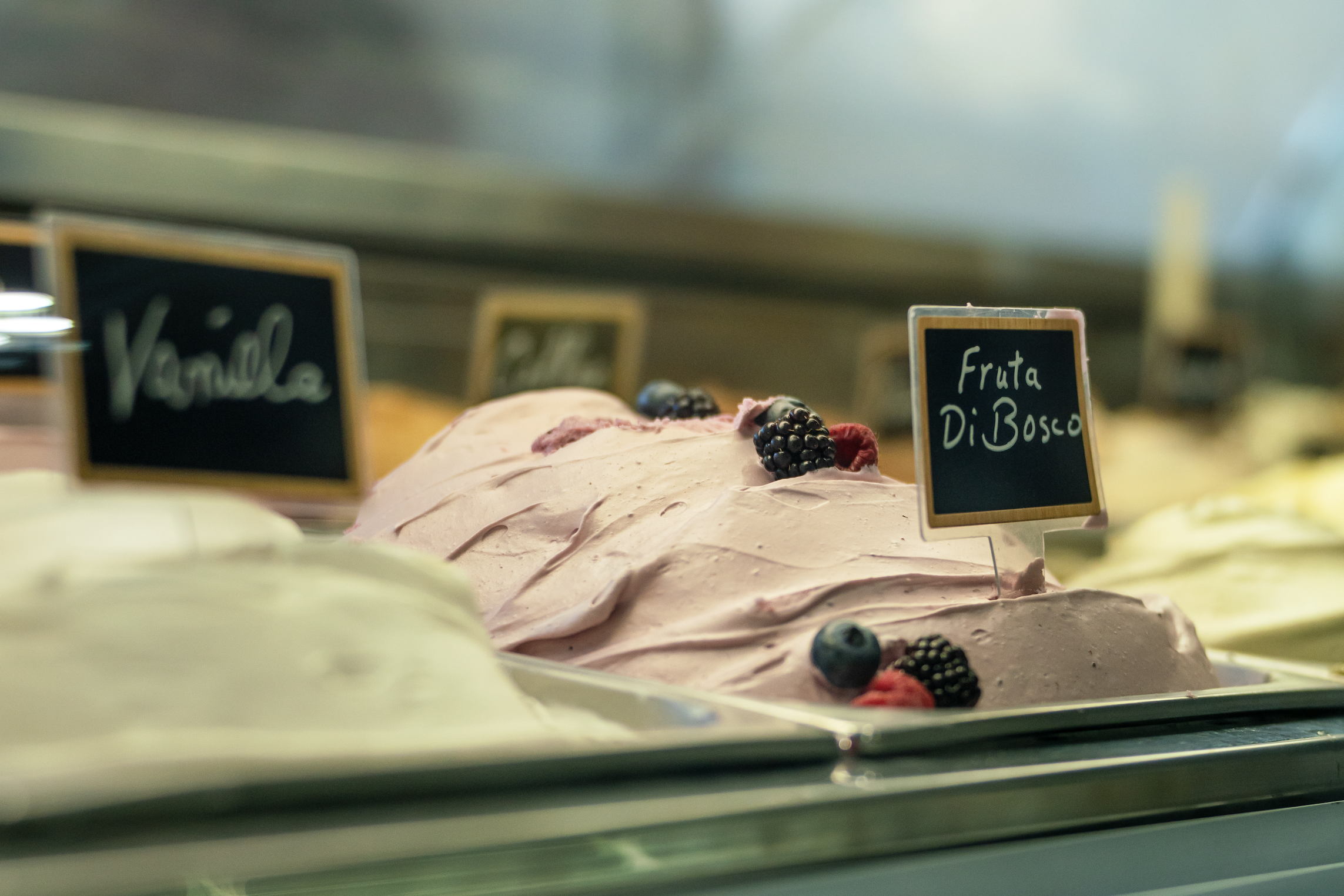 Various flavors of gelato ice cream in a display case, with small chalkboard signs labeling the flavors.