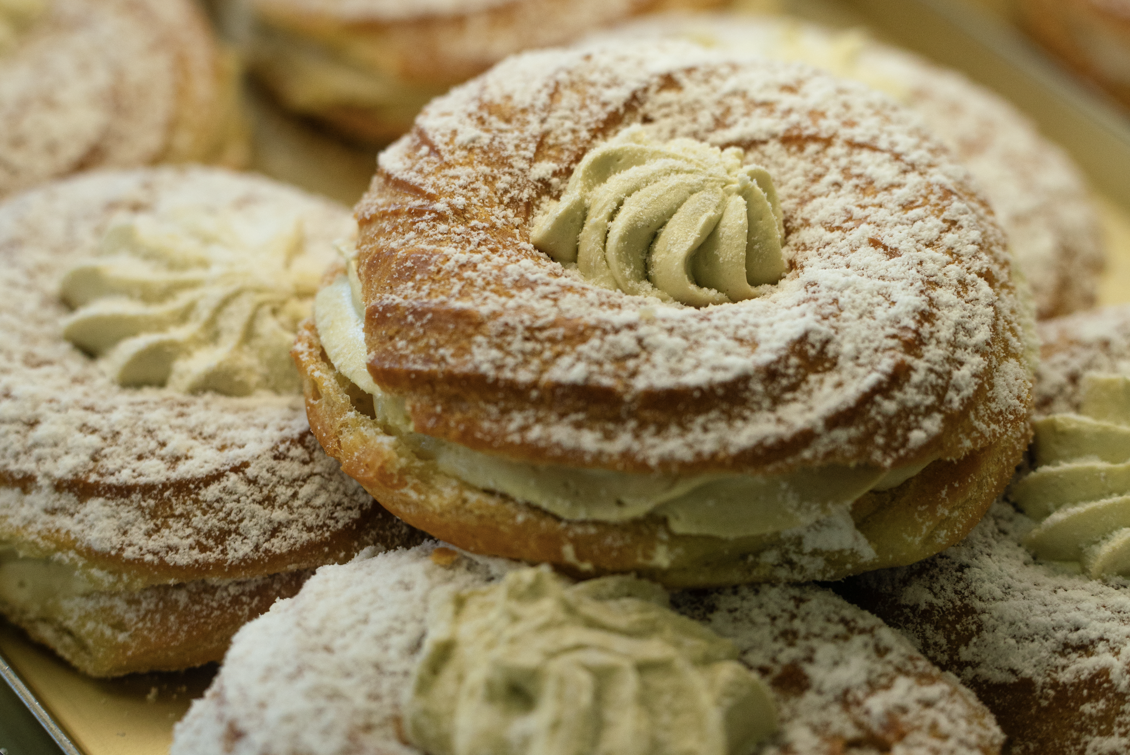 Close-up of several cream-filled pastries topped with powdered sugar and small dollops of cream.