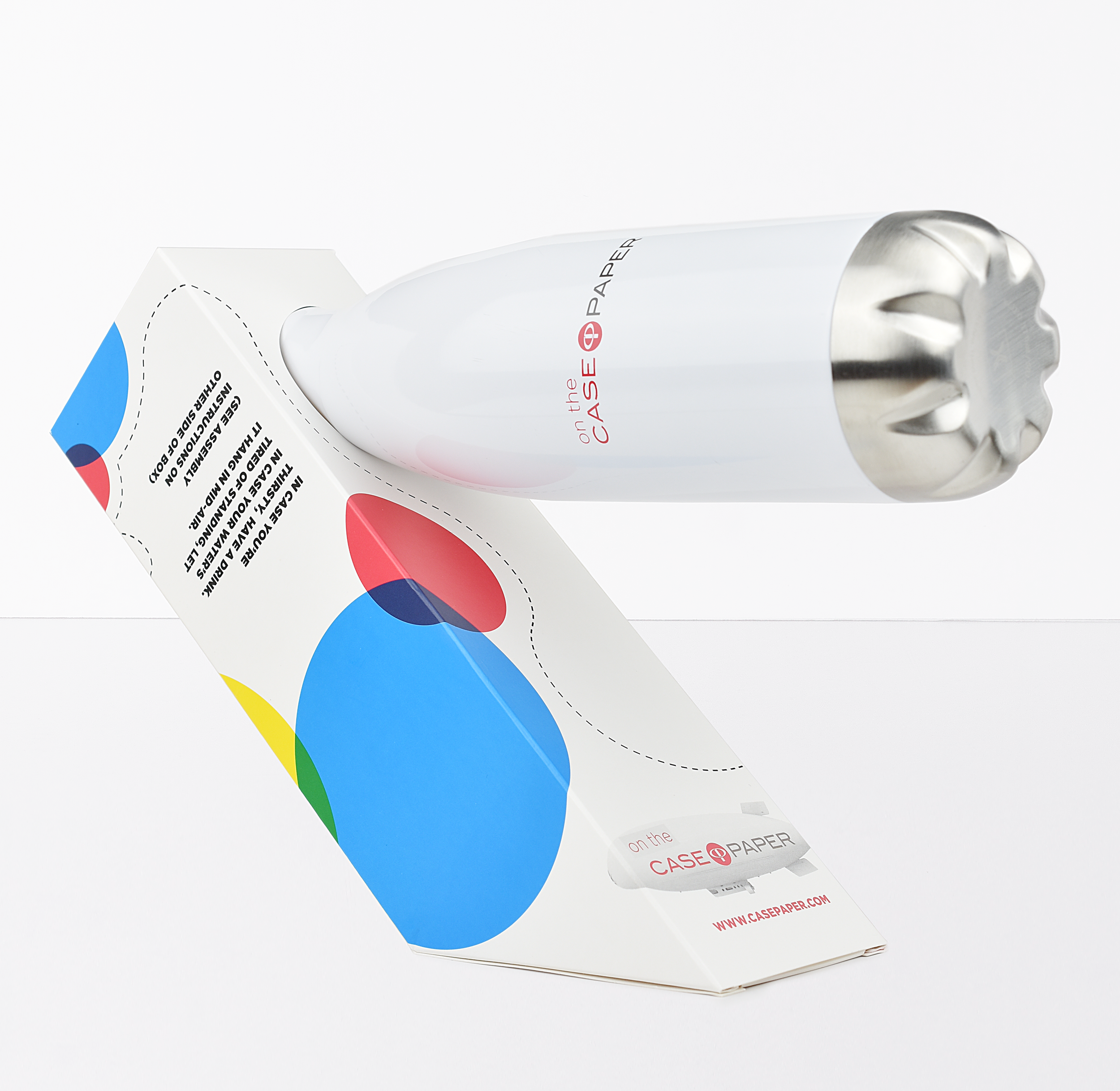 A paper shredder designed as a white capsule with metallic top, shredding colorful paper in red, blue, green, yellow, and white, with the brand name 'on the CASE PAPER' printed on it.