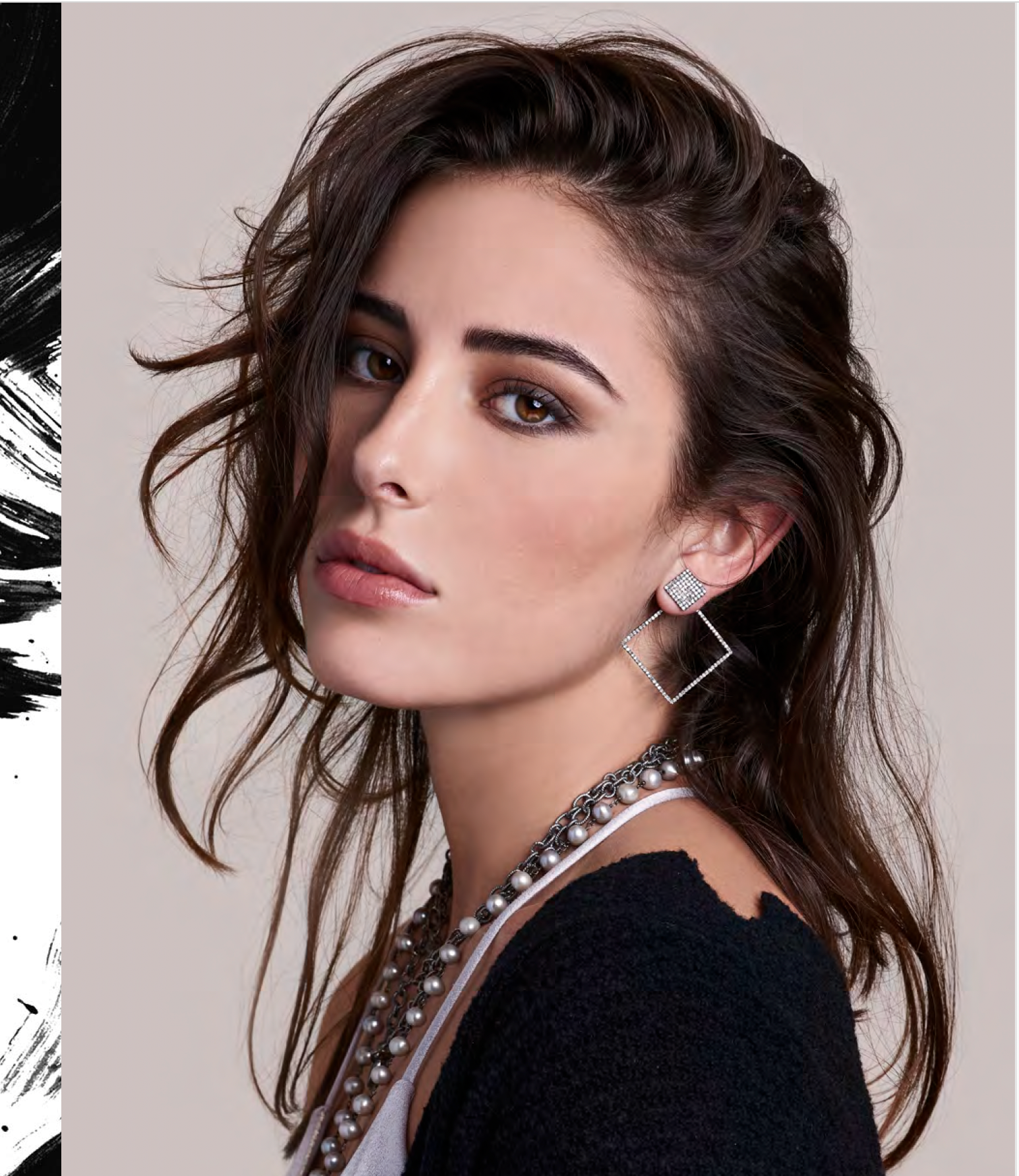 A woman with wavy dark brown hair and brown eyes wearing silver square and diamond earrings and layered pearl necklaces