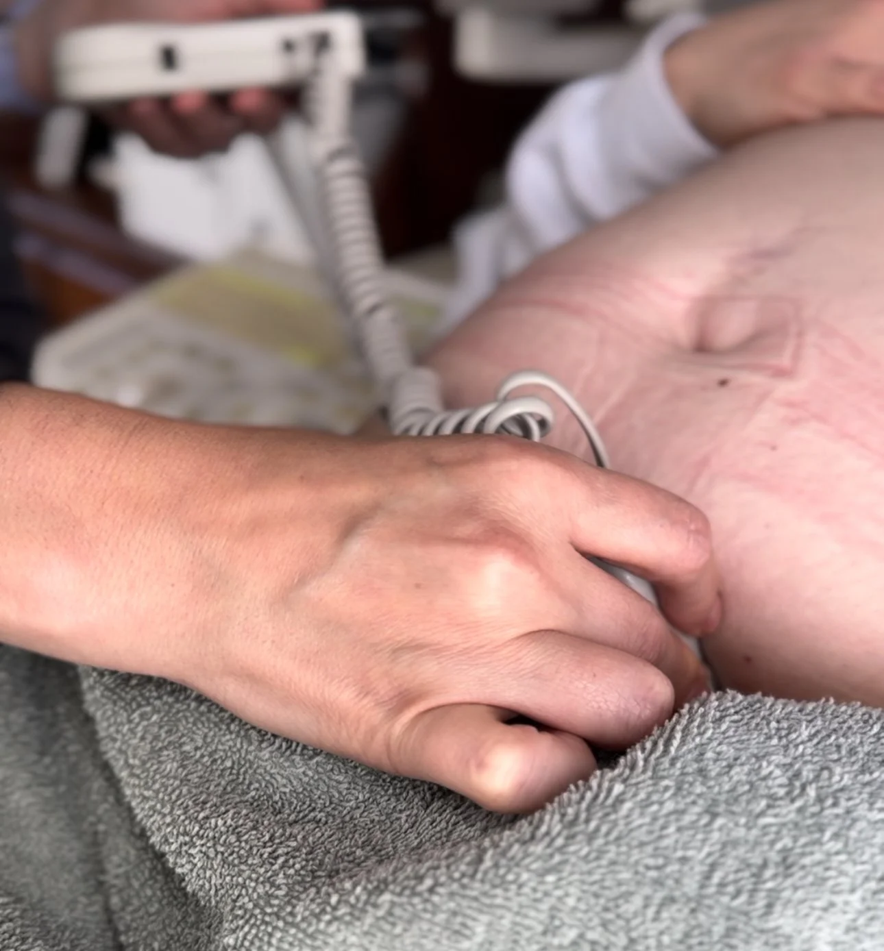 A midwife holding fetal heart doppler on a patient's belly lying down in office with ultrasound machine nearby