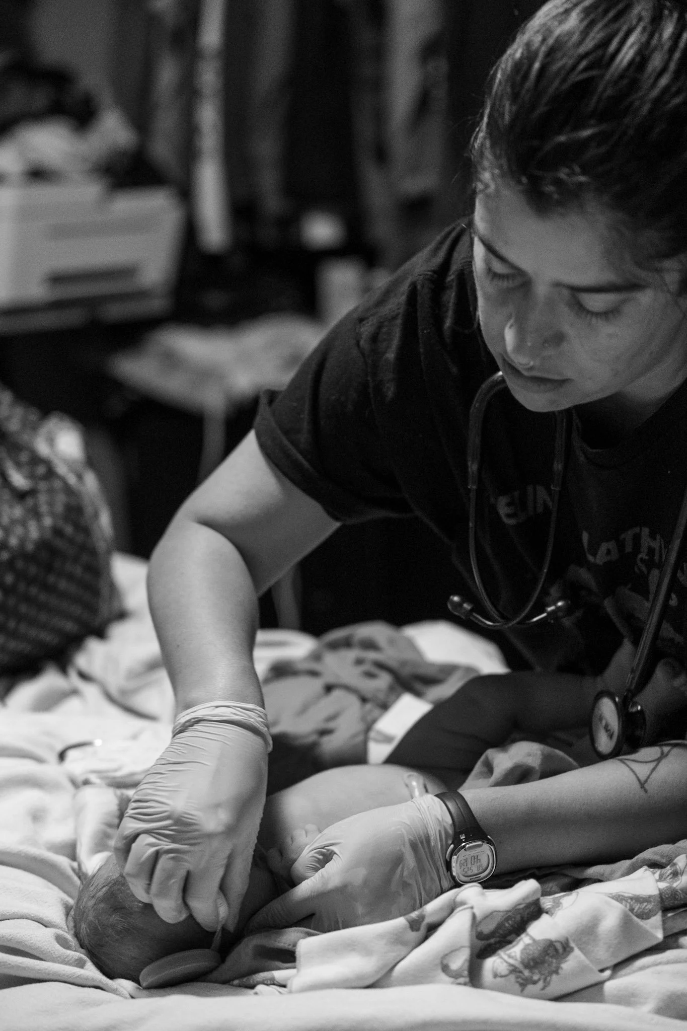 A midwife wearing gloves gently caring for a newborn baby on a bed.