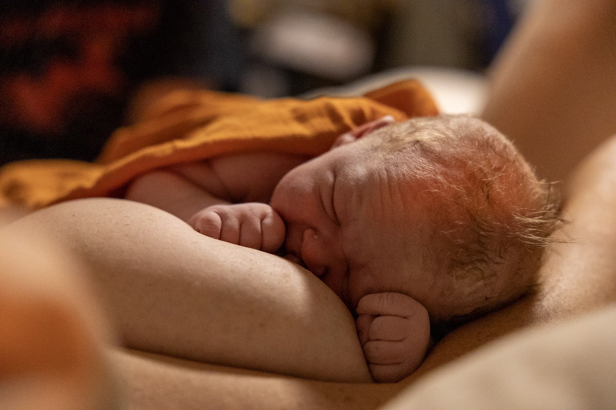 Close-up of a newborn baby breastfeeding, with the baby’s face rubbed against the mother’s breast and tiny hand clenched.