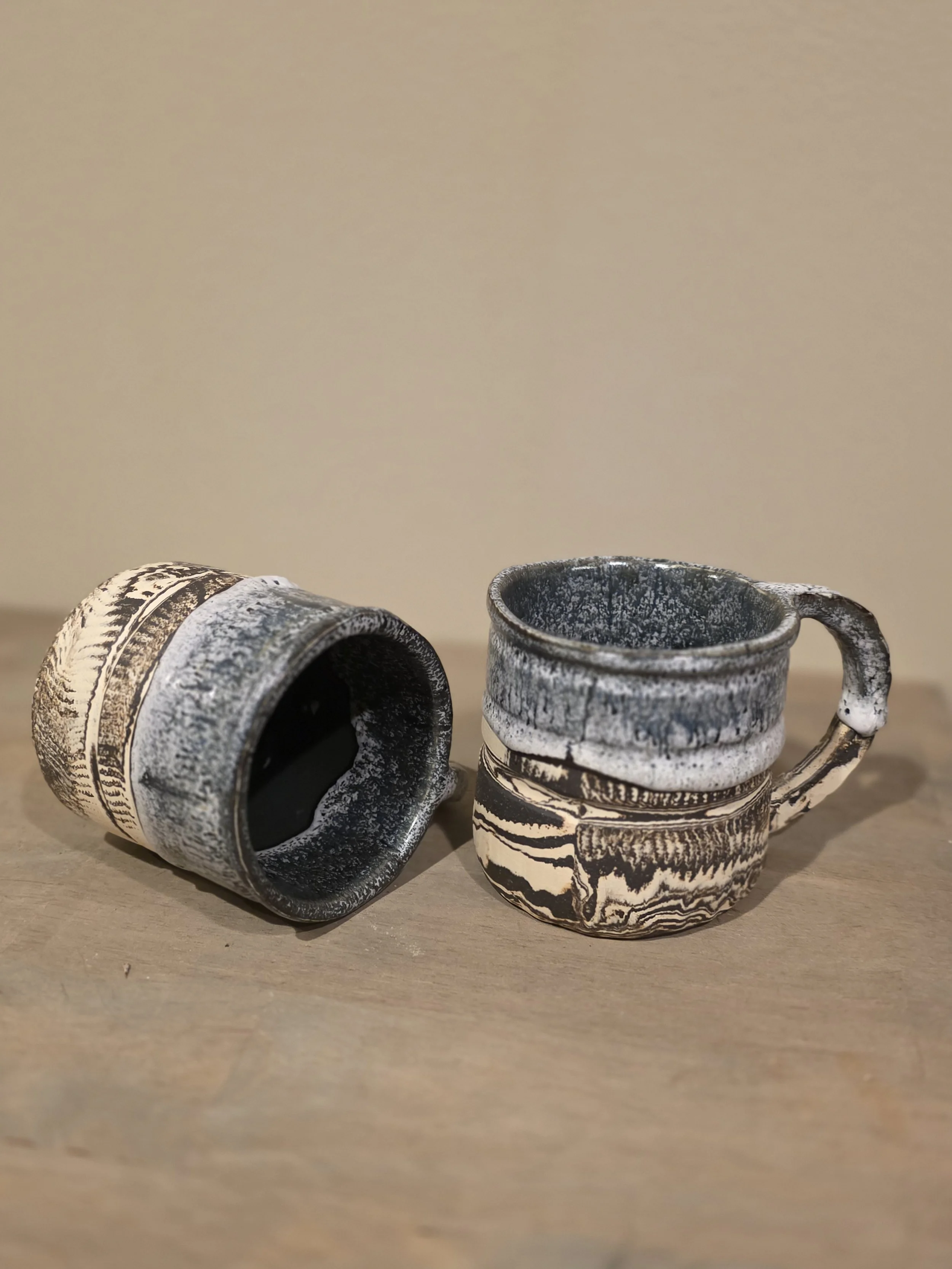 Two ceramic mugs with black, white, and gray marbled patterns on a wooden surface.