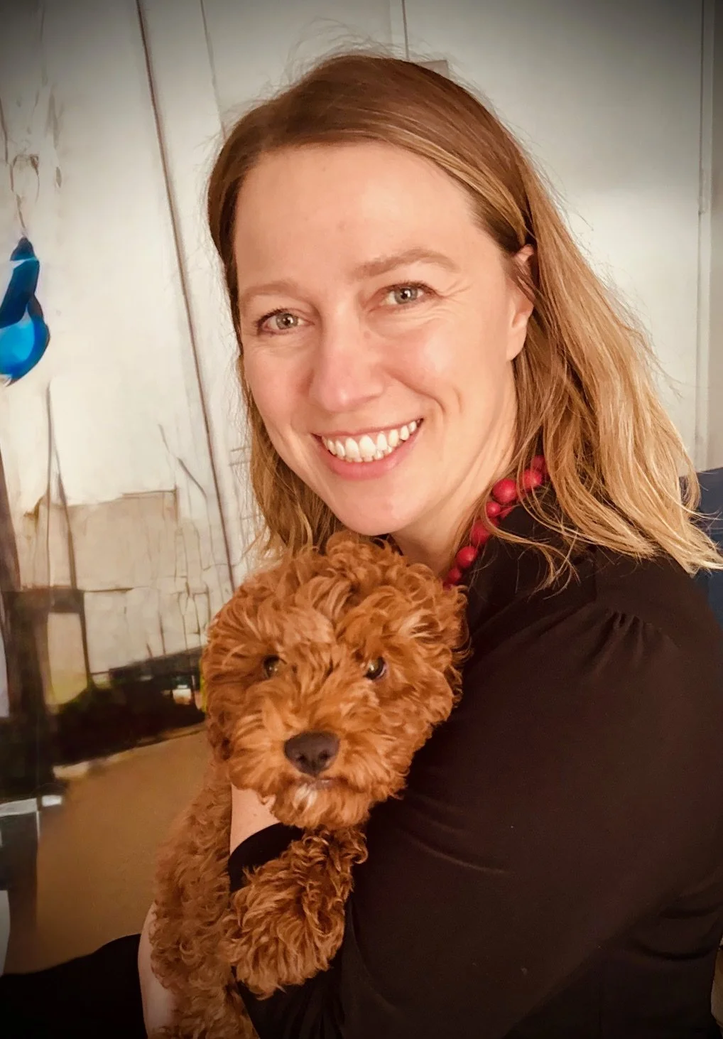 A woman with shoulder-length red hair smiling and holding a small, fluffy, reddish-brown puppy.