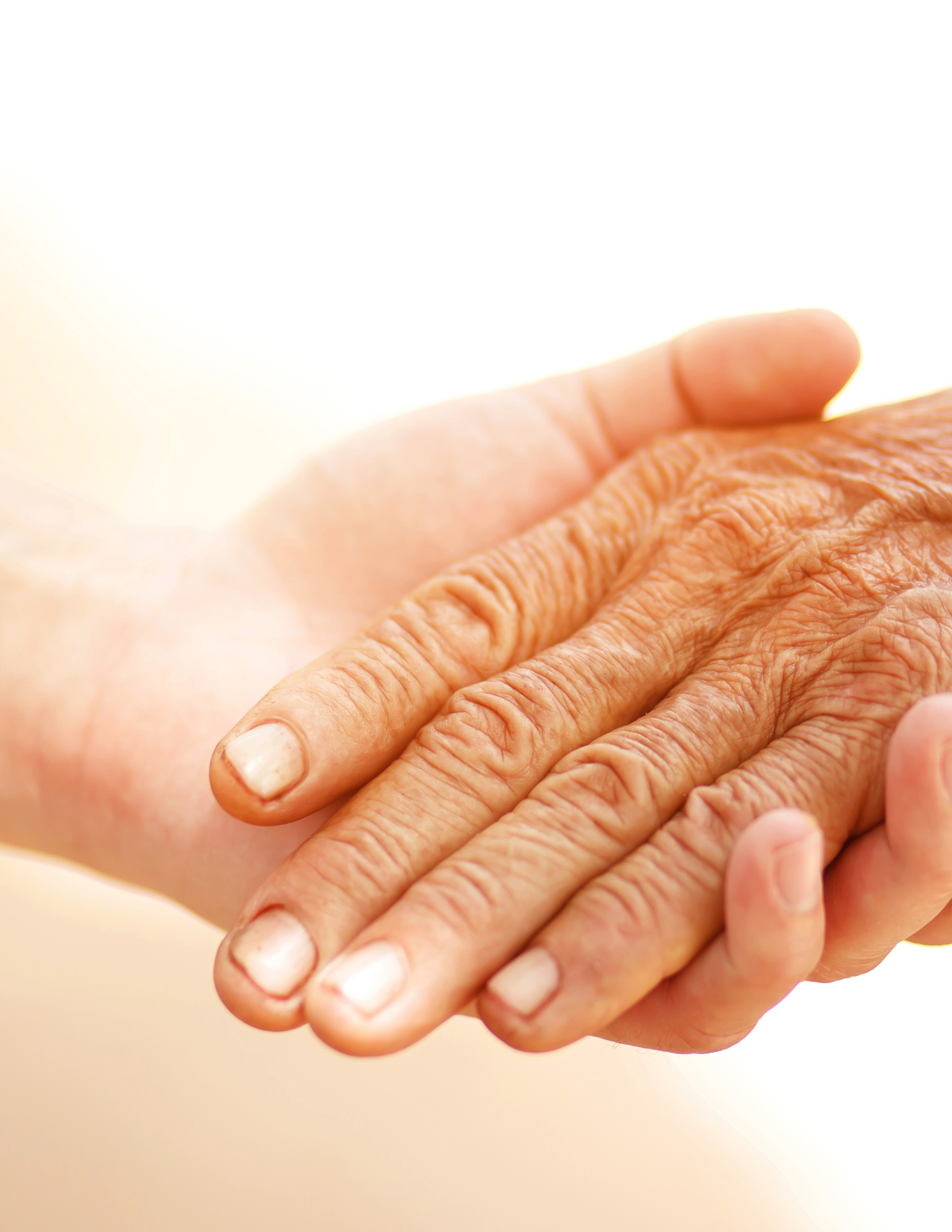 Close-up of two hands, one elderly with wrinkled skin and the other younger, gently holding each other.