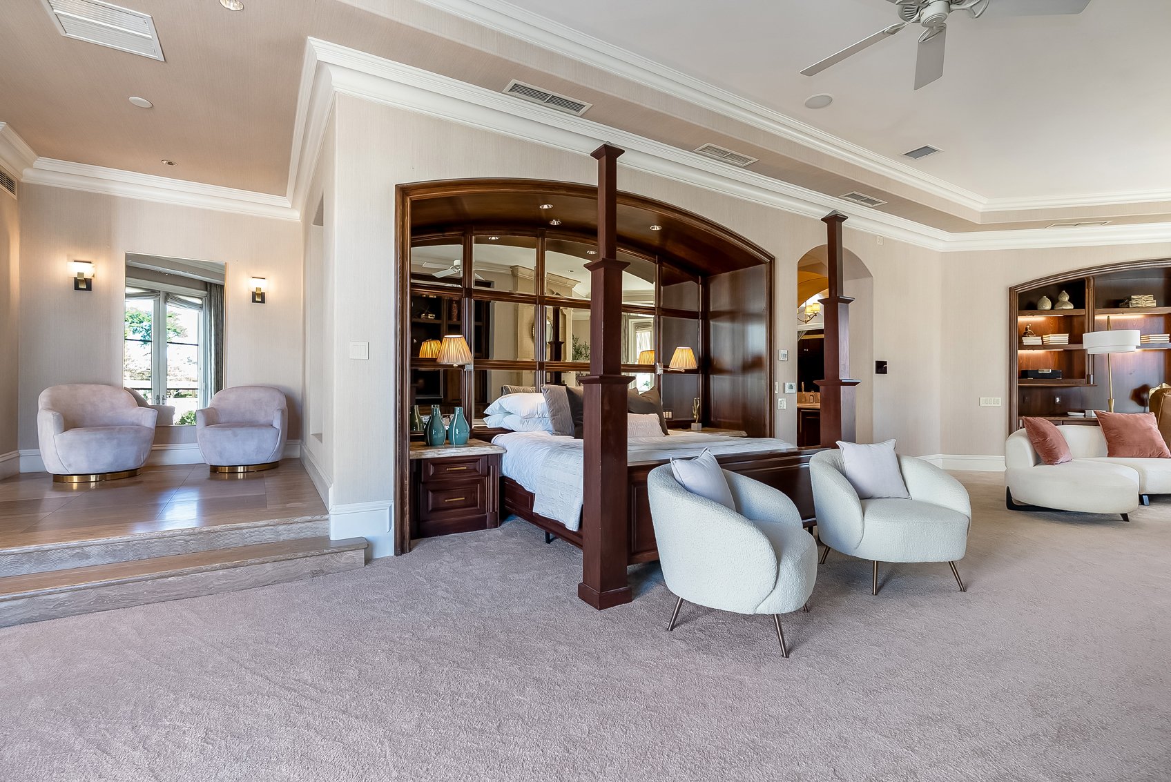 Luxurious bedroom with an open layout, featuring a four-poster bed, armchairs, built-in bookshelves, and elegant lighting.