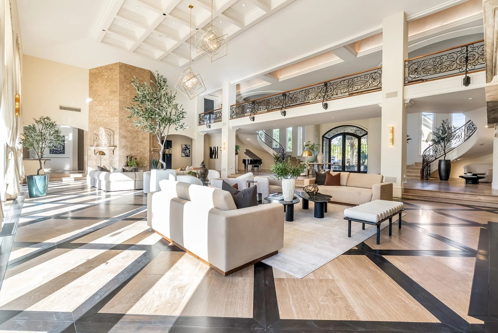 spacious, elegant lobby with high ceilings, large windows, and modern decor including white and beige furniture, potted plants, a grand staircase, and decorative lighting fixtures.