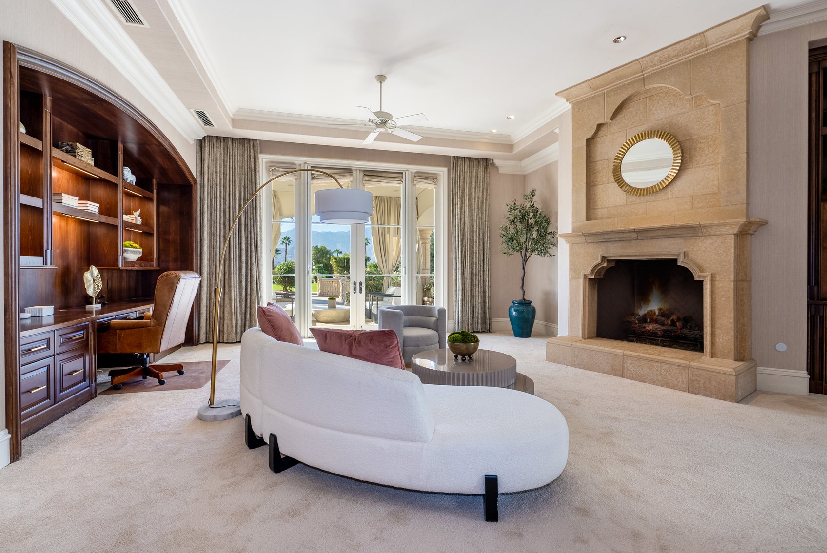 Elegant living room with fireplace, large windows, and outdoor view, decorated with modern furniture and a bookshelf.
