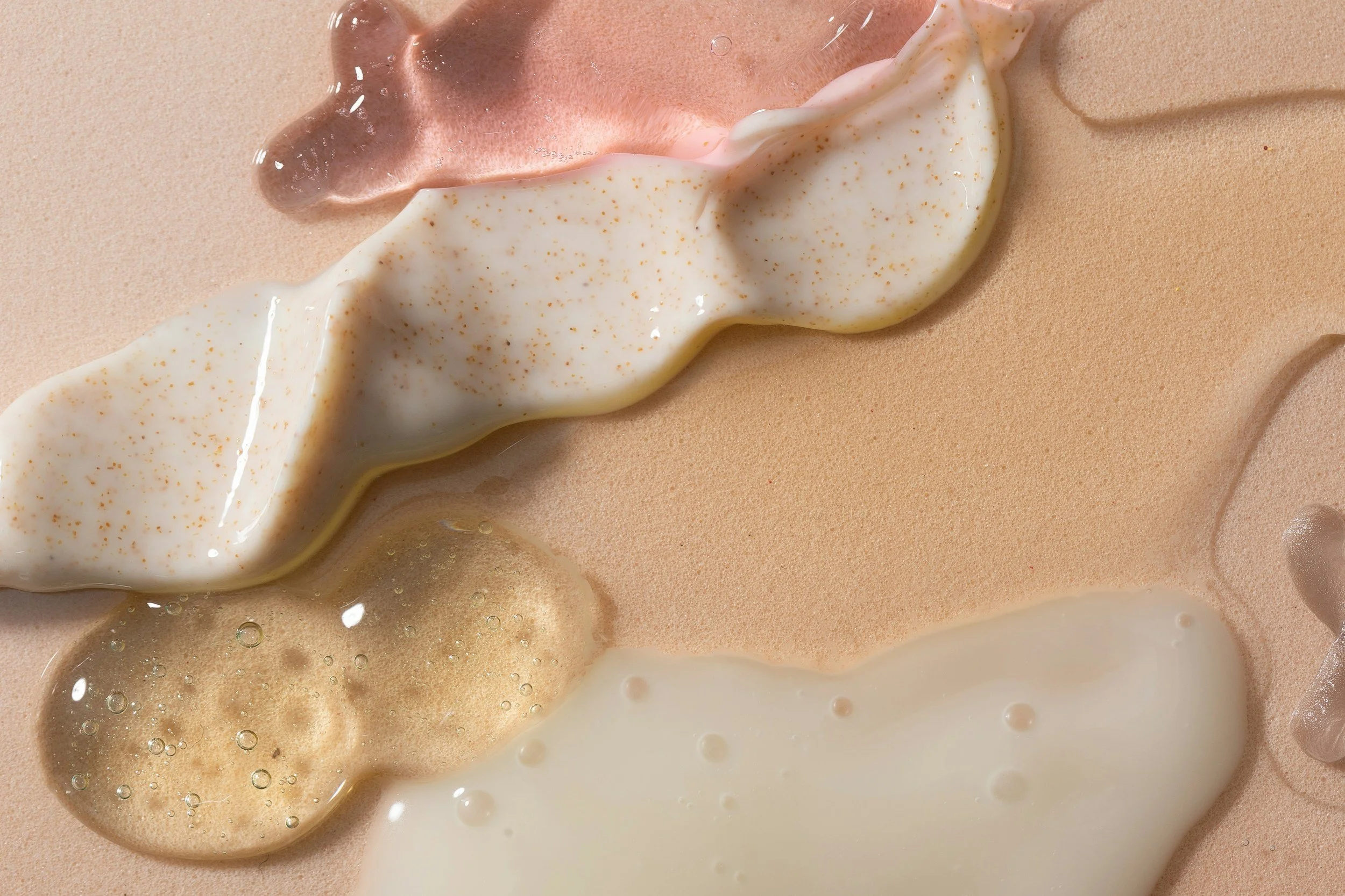 Various textured liquids on a beige surface, including white, pink, and brownish substances, with some parts appearing foamy or bubbly.
