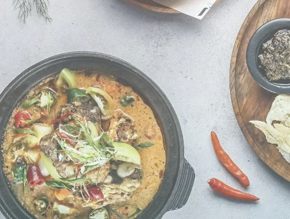 A bowl of Thai curry with vegetables and meat, accompanied by small chili peppers on a gray surface.
