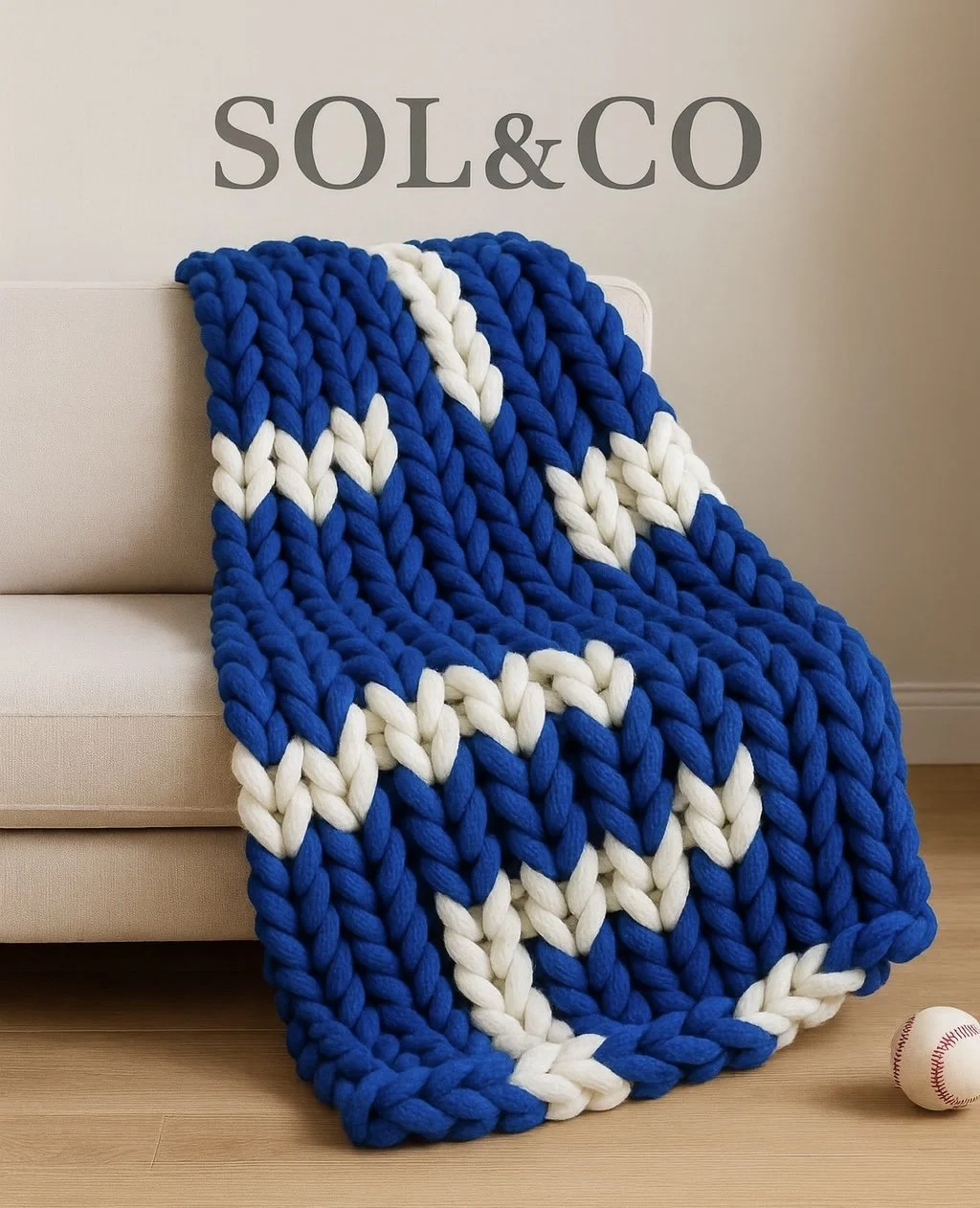 A chunky blue and white knit blanket draped over a beige sofa, with a baseball on the floor nearby, and the word 'SOL&CO' on the wall behind.