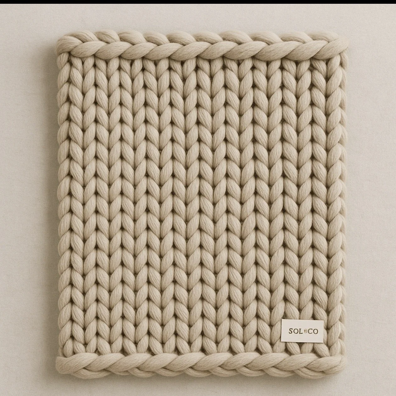 A beige chunky knit blanket with a small SOL&CO label in the bottom corner, displayed against a plain white background.