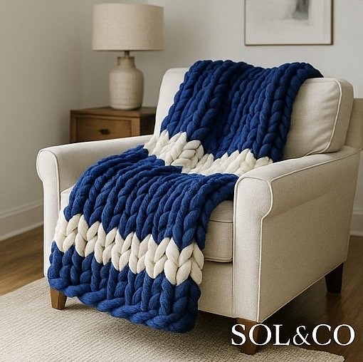 A chunky blue and white knitted blanket draped over a white armchair in a cozy living room setting.