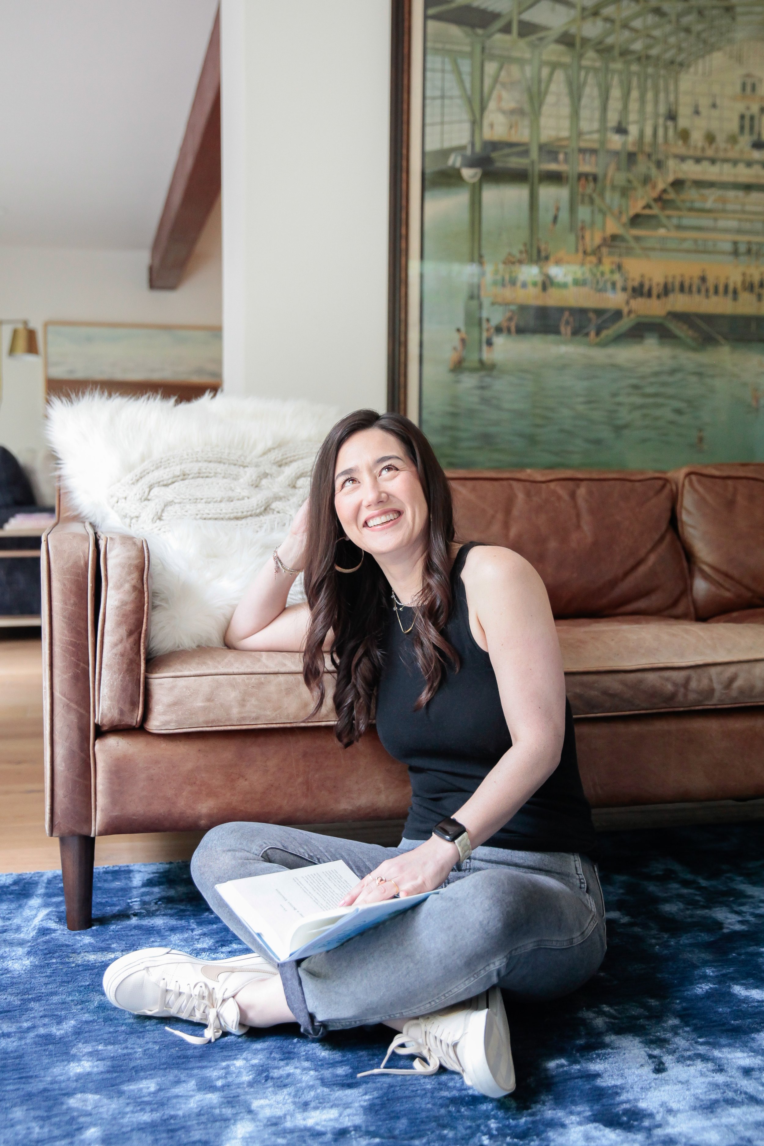 The Warm Edit founder seated on the floor with a book in a living space.