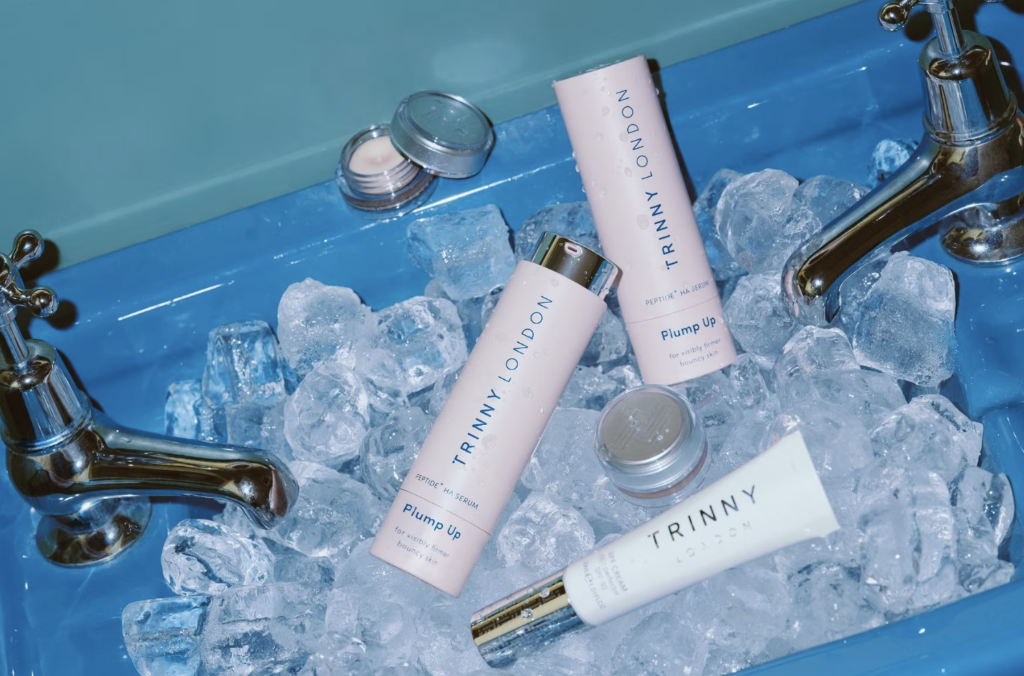 Skincare products from Trinny London on ice in a blue basin, including serums and creams.