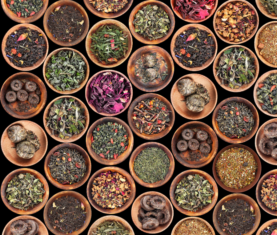A collection of small wooden bowls filled with various types of loose leaf teas and dried herbs, arranged in a closely packed pattern.