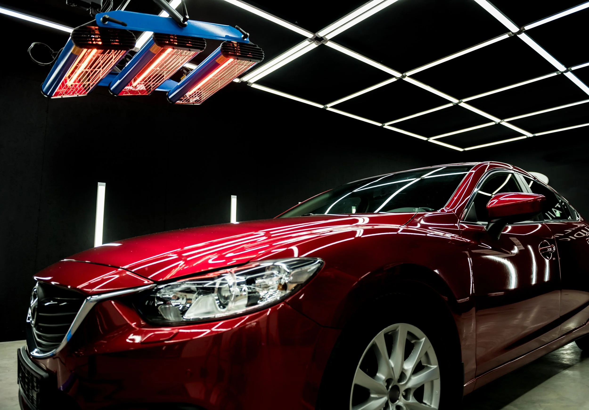 Red car inside a showroom with black walls and LED light ceiling, illuminated by neon lights.