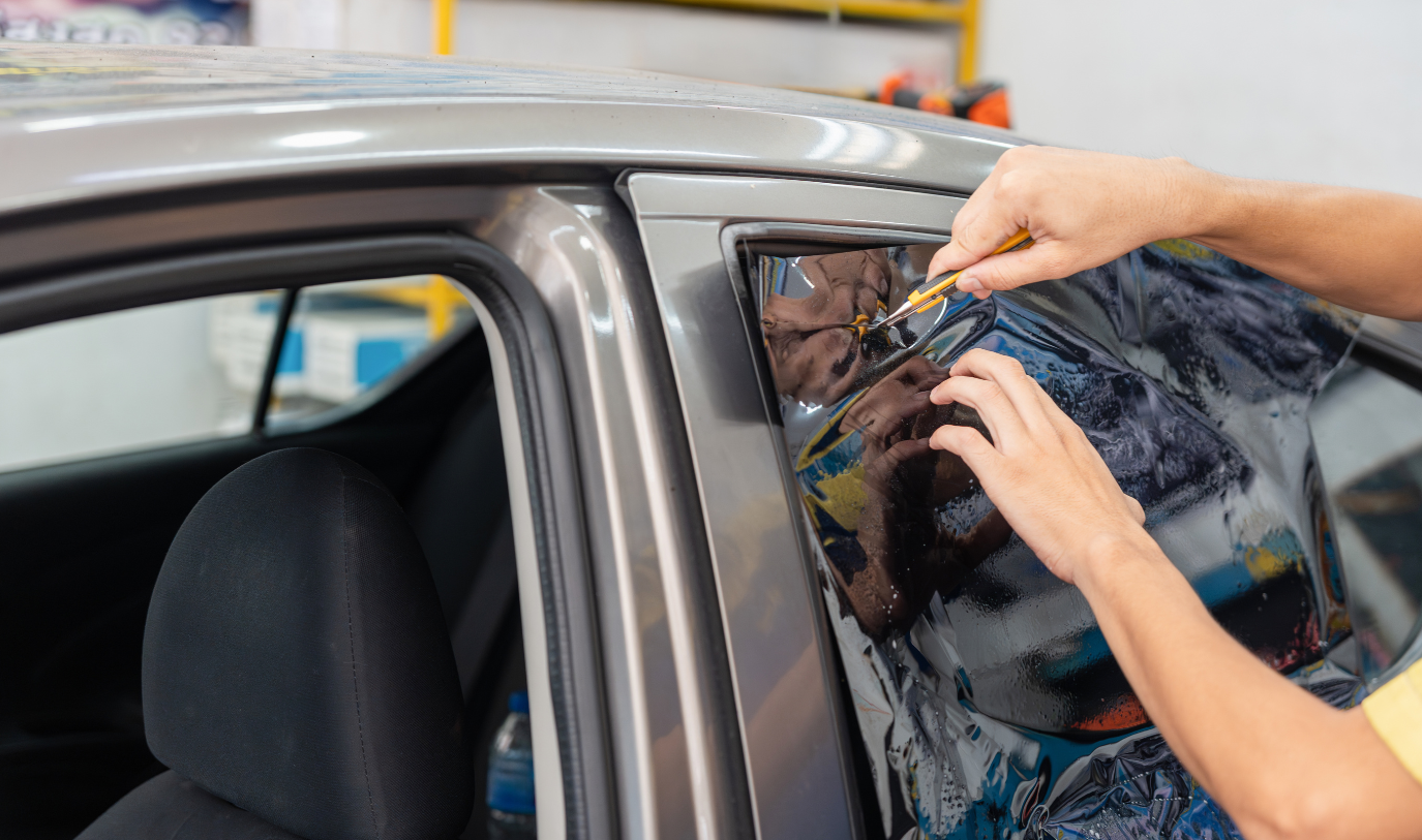 A person applying a protective film to a car's window in a workshop.