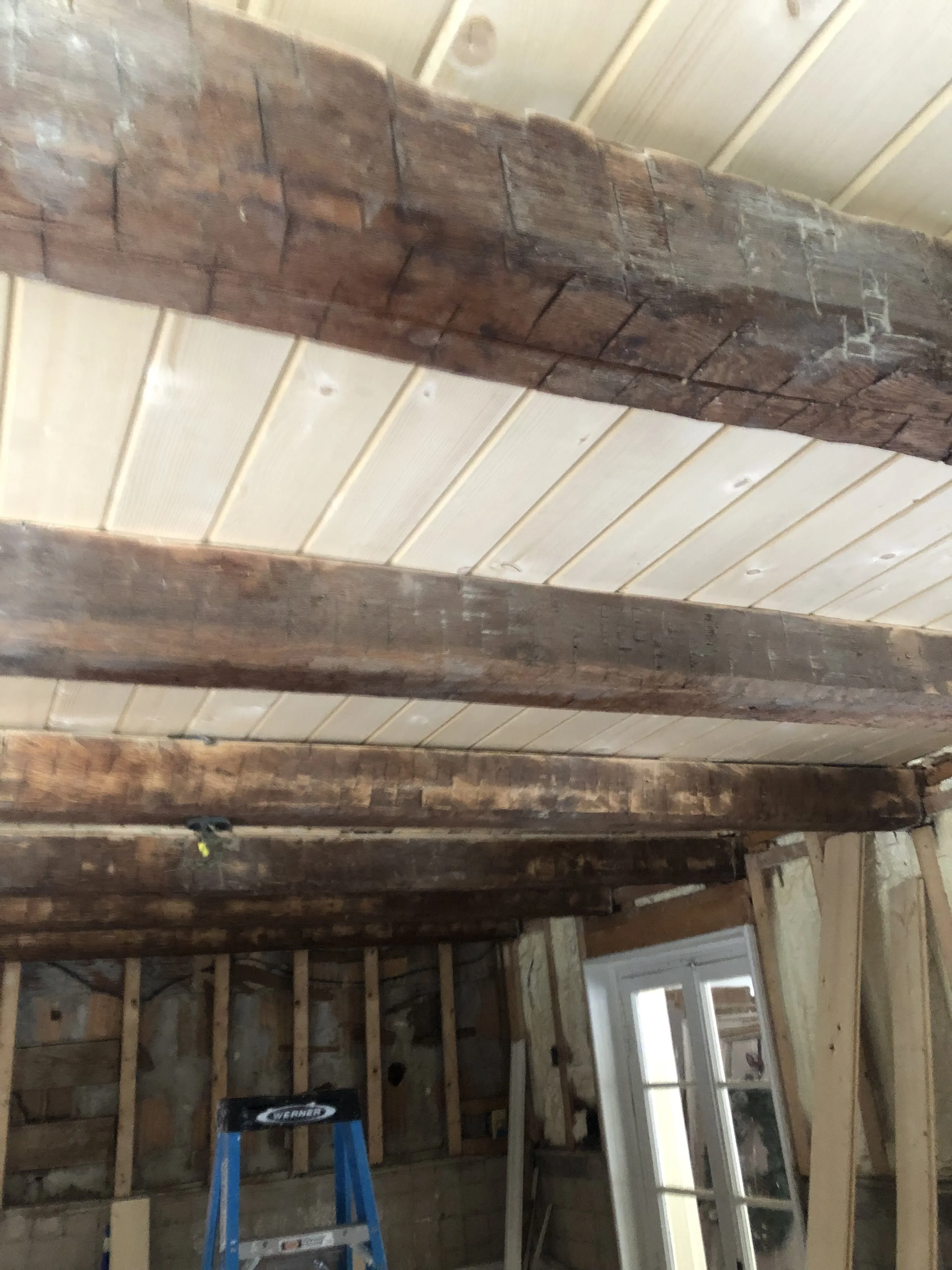 Construction site interior with exposed wooden beams, wall studs, and a window, indicating ongoing renovation or building process.