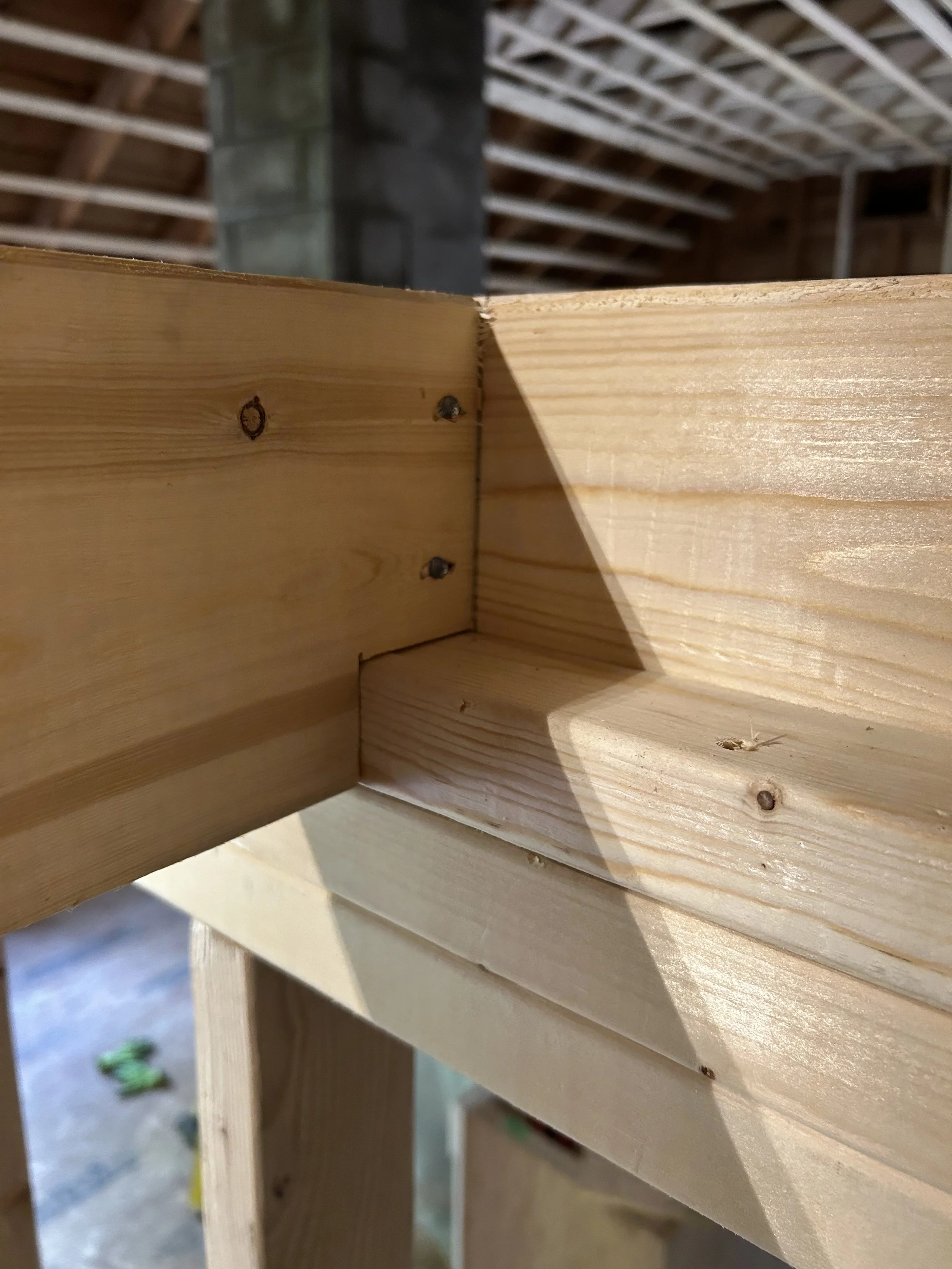 Close-up of a wooden construction joint in a building under construction, showing the corner of a wooden frame with nails, with an unfinished background of the garage or attic interior.