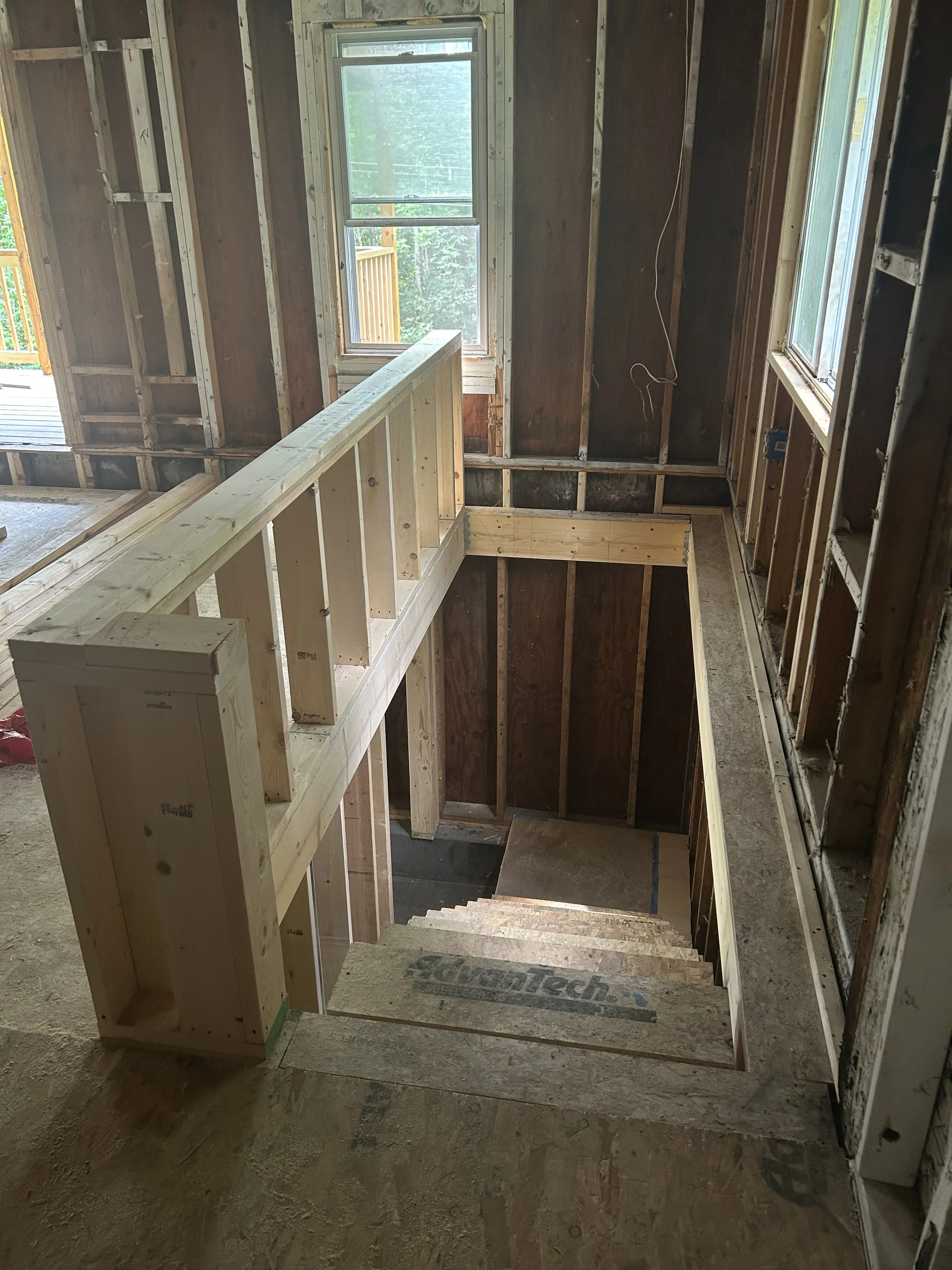 Interior of a house under construction, showing stairs and framing with unfinished walls and windows.