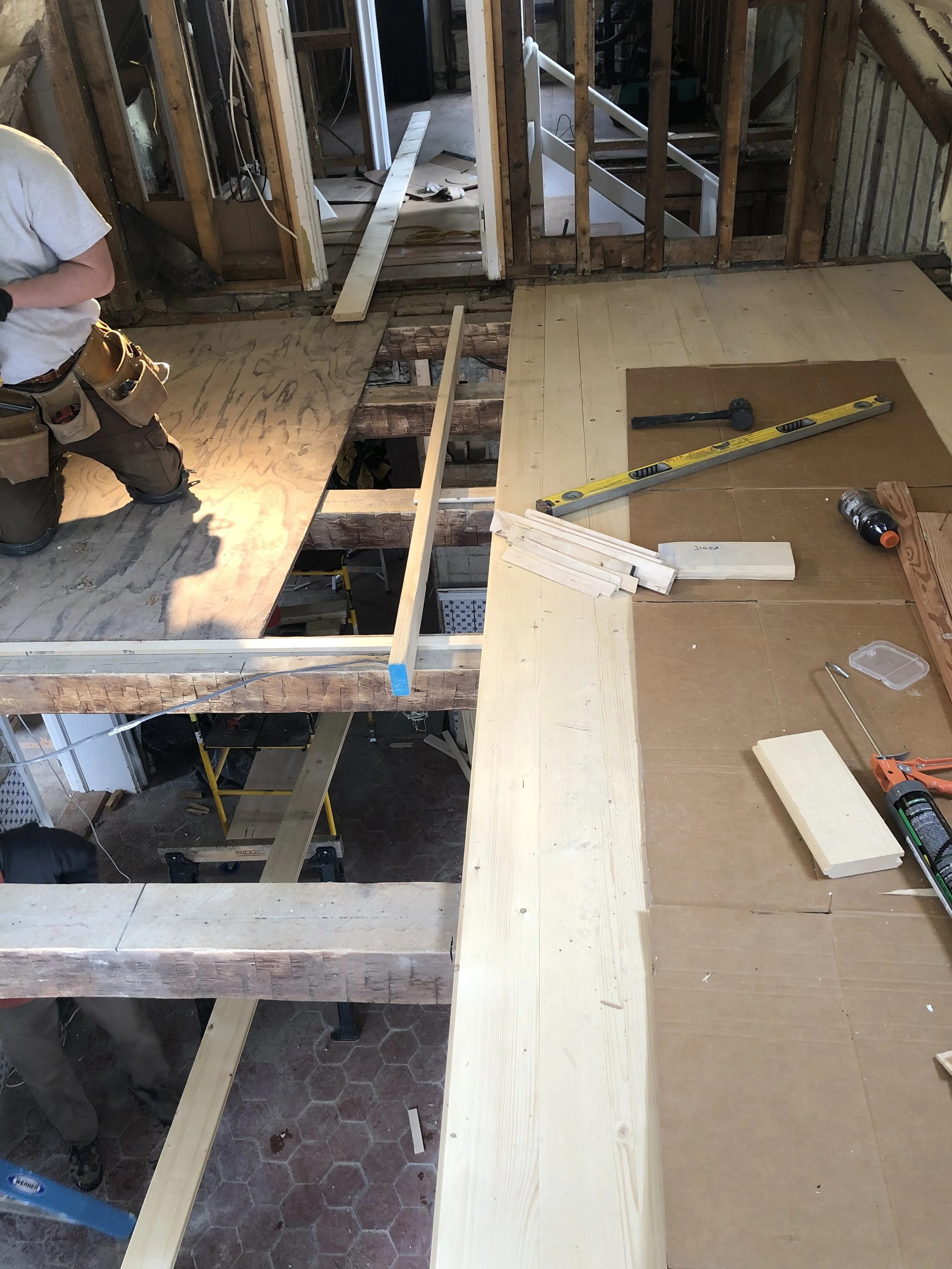 Interior view of a construction site showing flooring being installed with wooden planks, construction tools, and workers in progress.