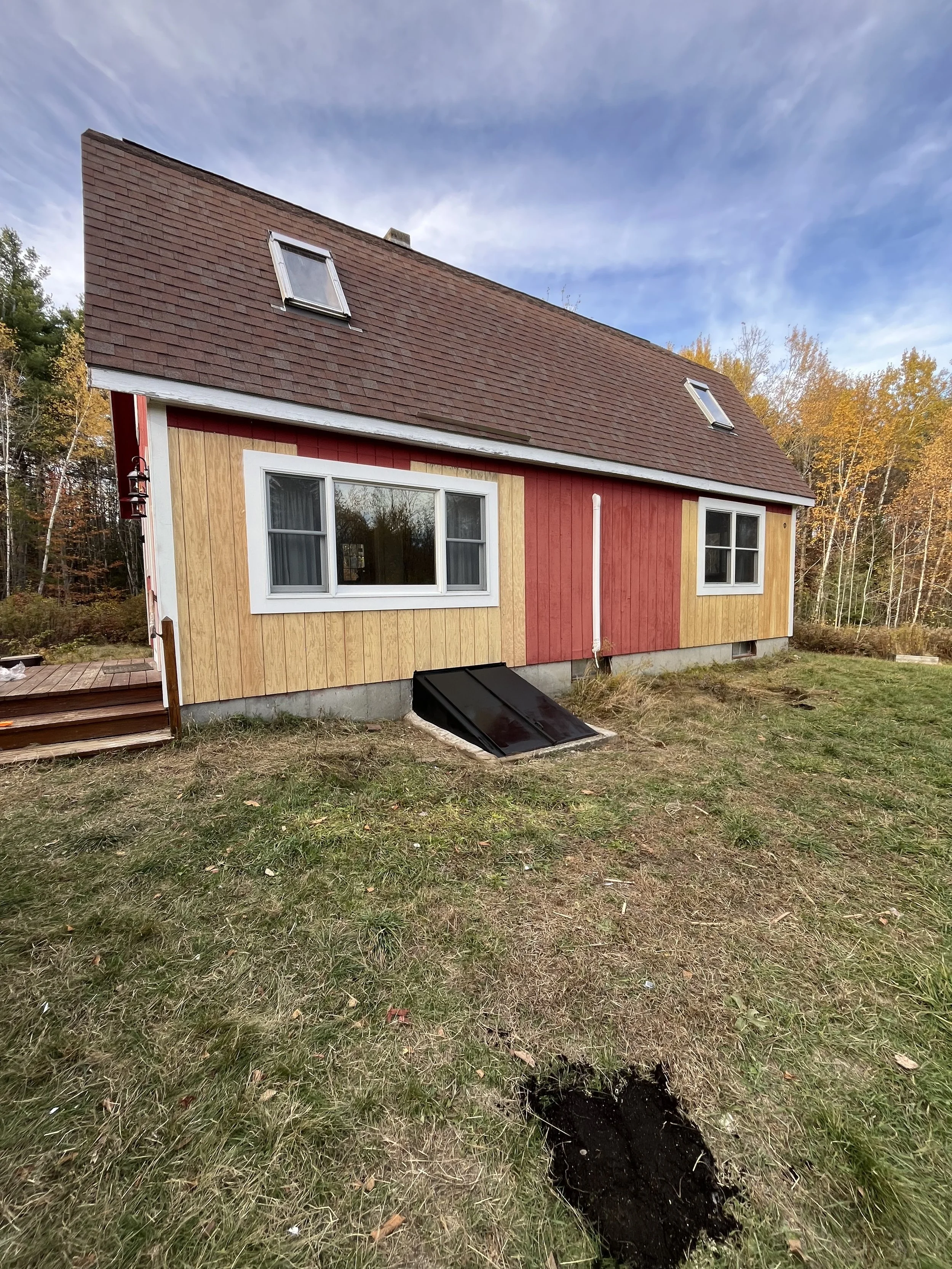 A house with a red and beige exterior, two dormer windows on the roof, and a partially dug hole in the front yard. General contractor. Carpentry.