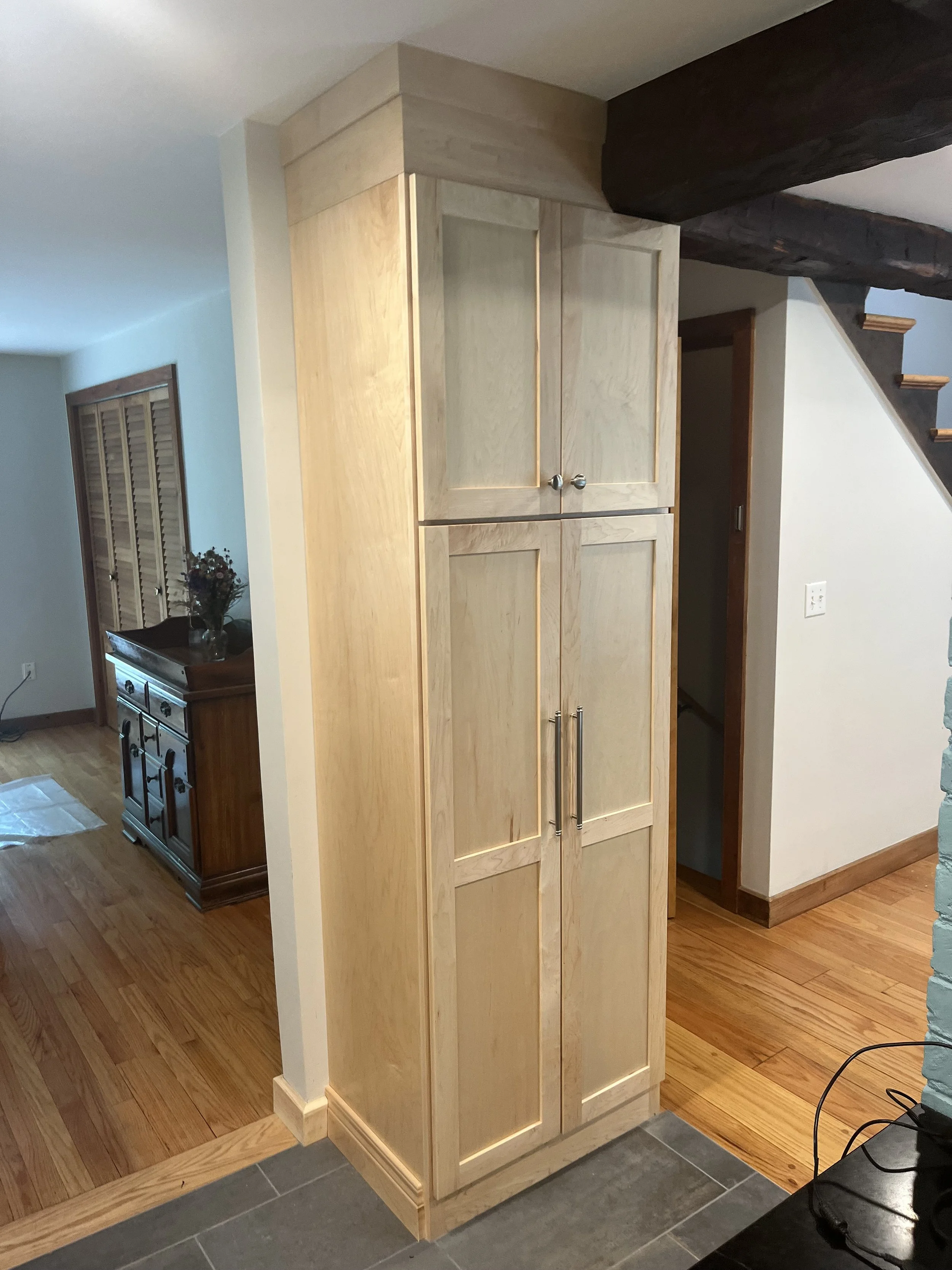 A tall, unfinished wooden cabinet with two doors and metal handles in a home interior.
