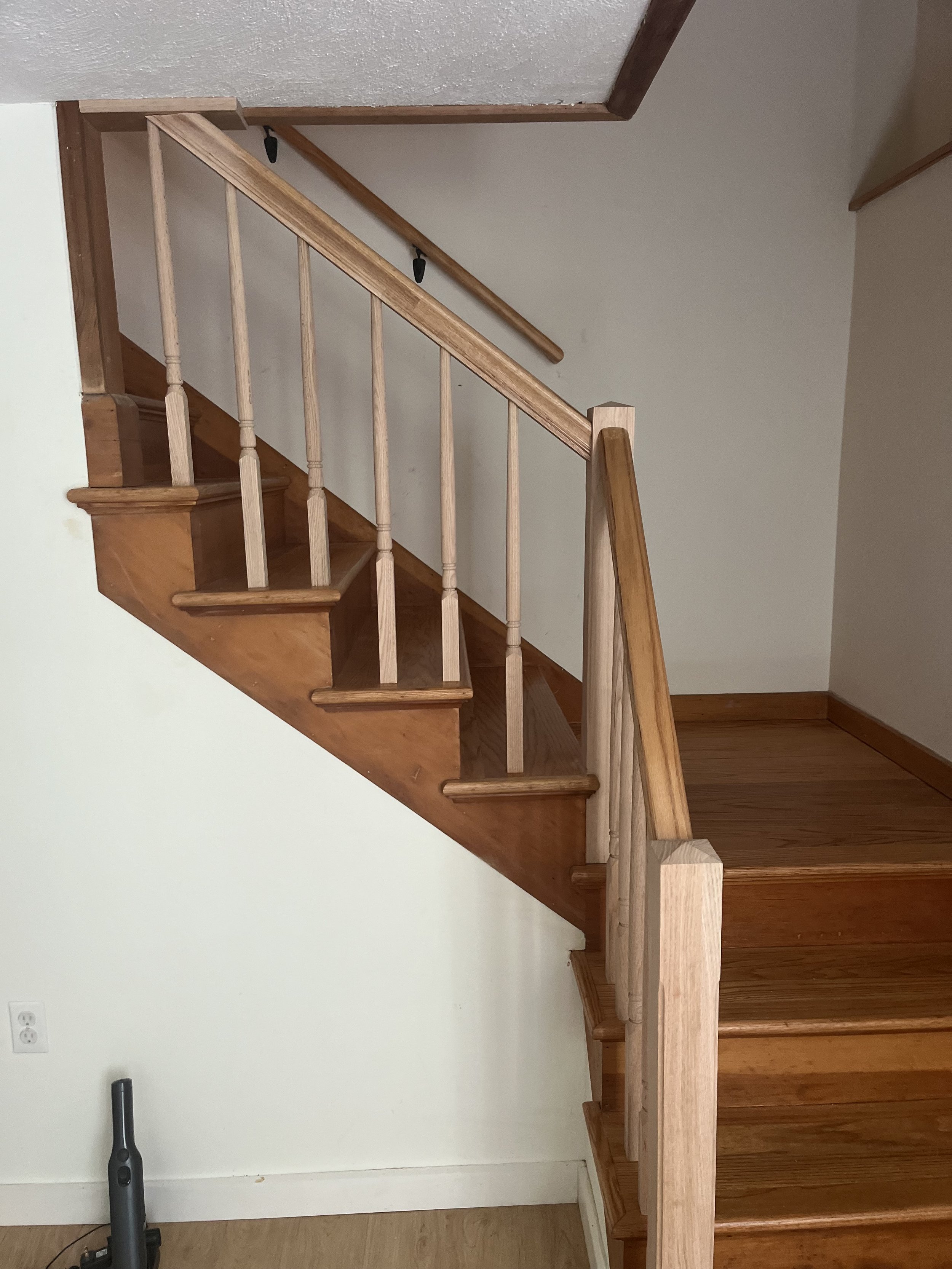 Wooden staircase with railing leading to upper level in a home interior, with a vacuum cleaner on the floor below.