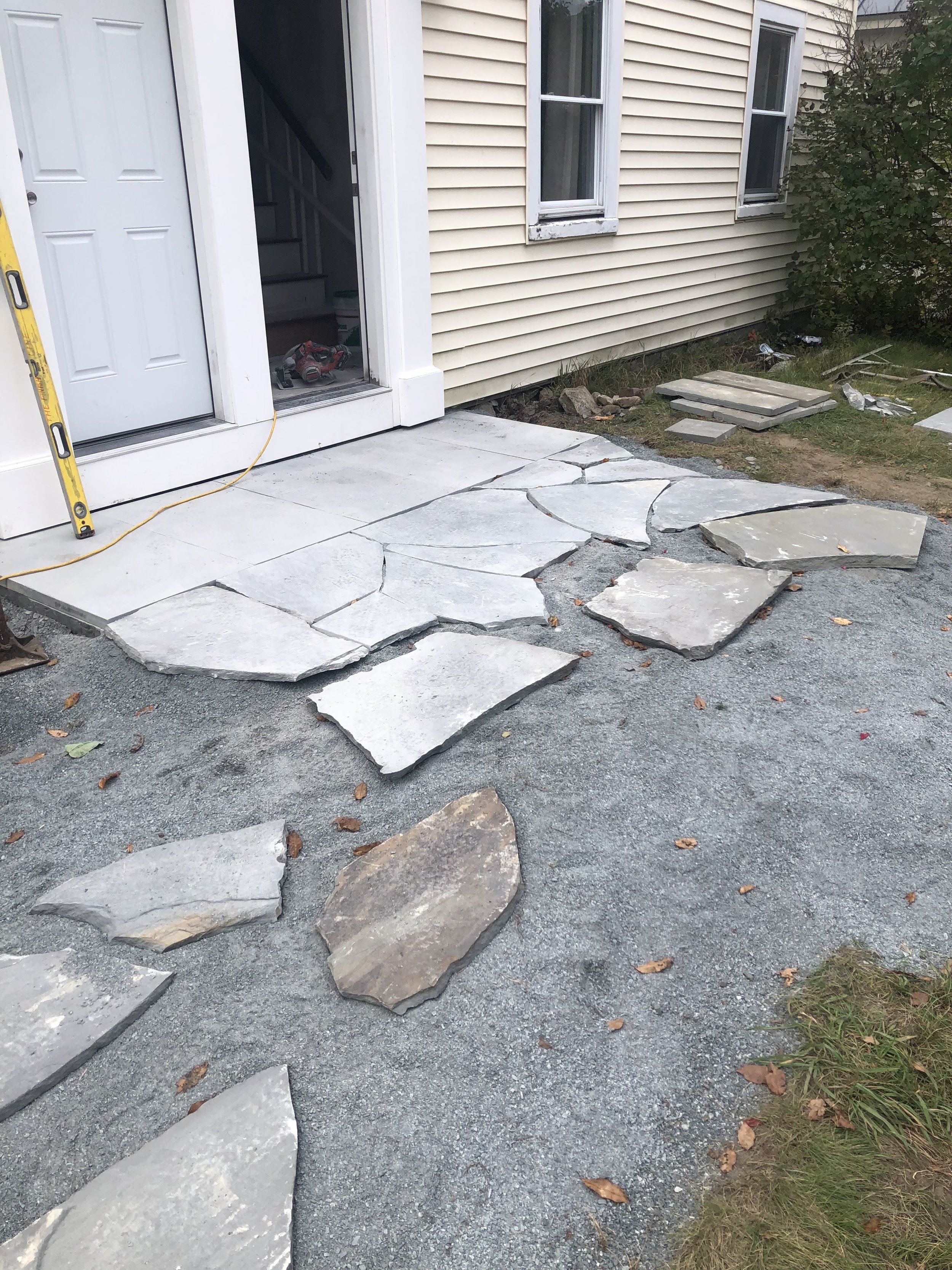 Unfinished stone patio installation outside a house, with flag stone slabs and construction tools. Hardscaping near me.