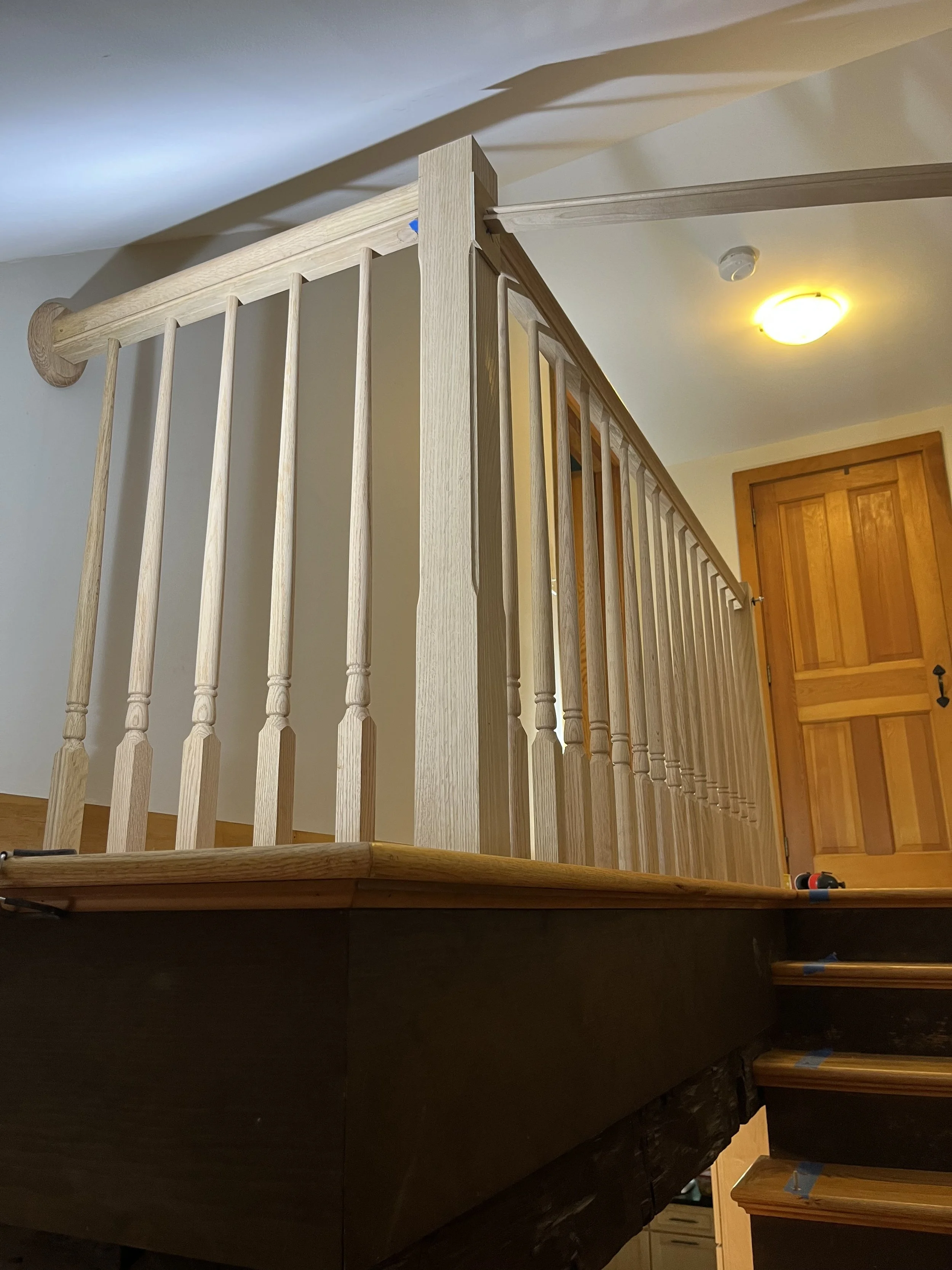 Wooden staircase with a newel post and spindles leading up to a landing and a closed wooden door in a residential interior with a ceiling light.