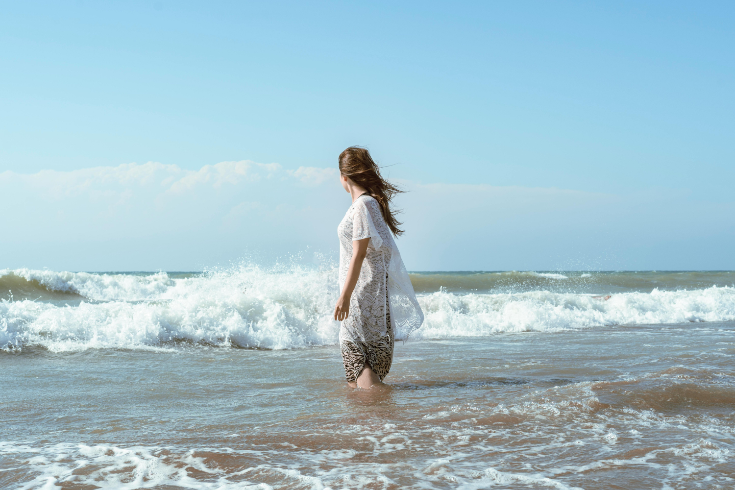 A peaceful silhouette of a person standing on a sandy beach as gentle waves flow around their feet, embodying the feeling of being an anchor in the middle of movement.
