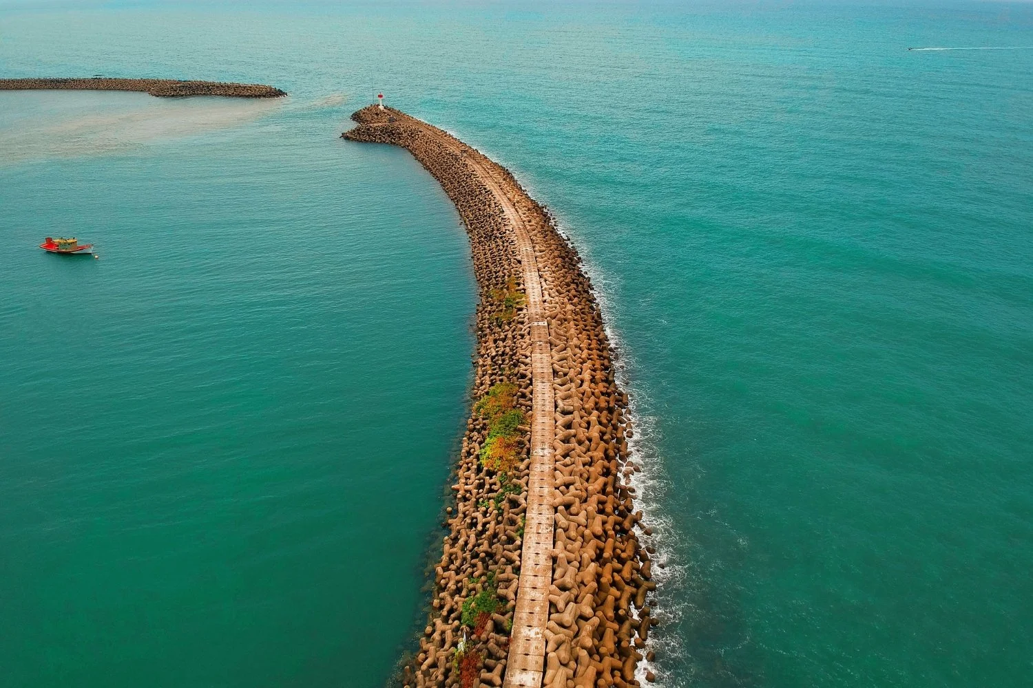 A wide stone coastal breakwater wall protecting calm still harbour water from choppy open ocean waves in soft autumn sunlight, representing routine as a sanctuary.