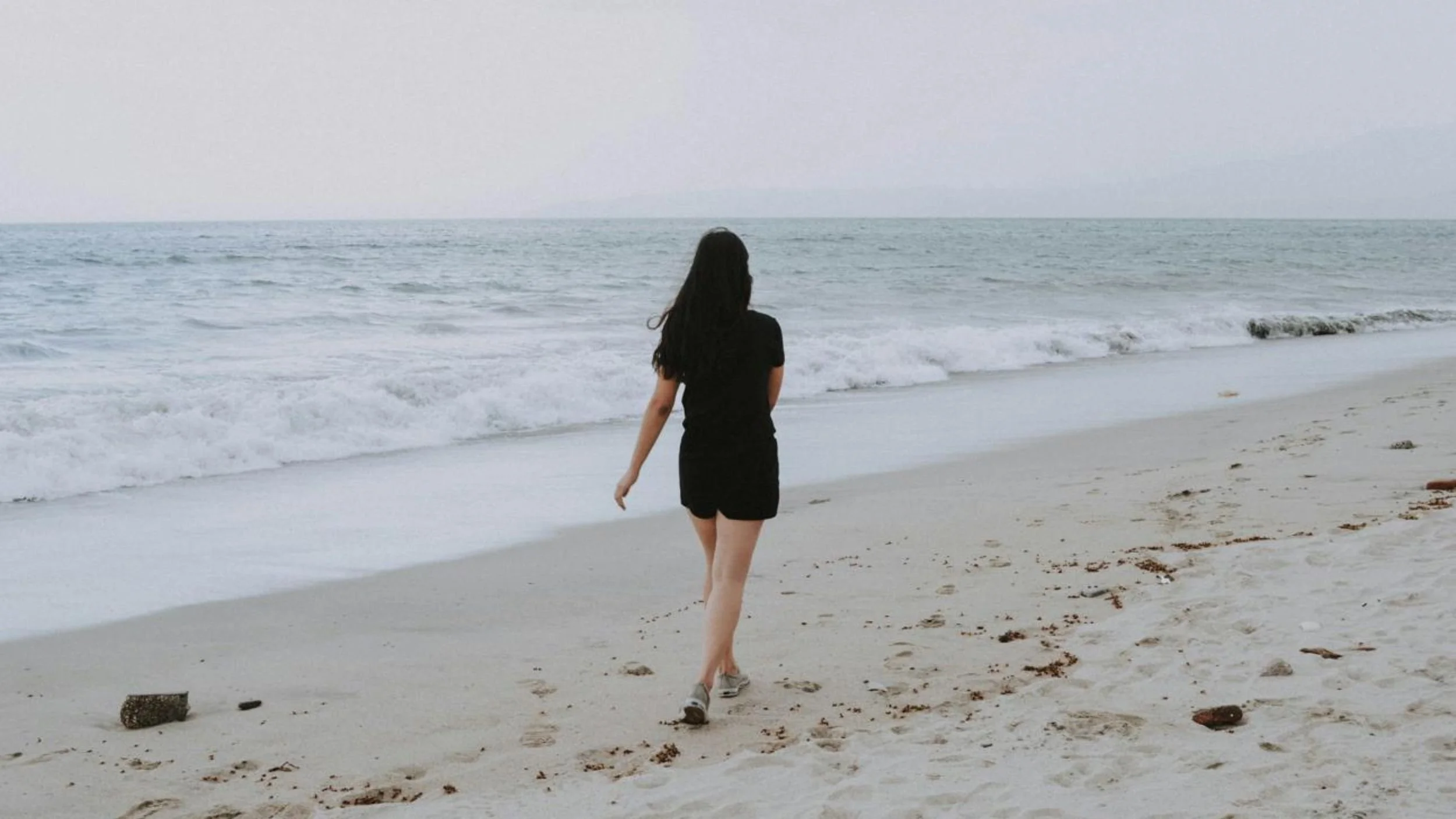 Woman walking alone along a quiet beach beside the sea.