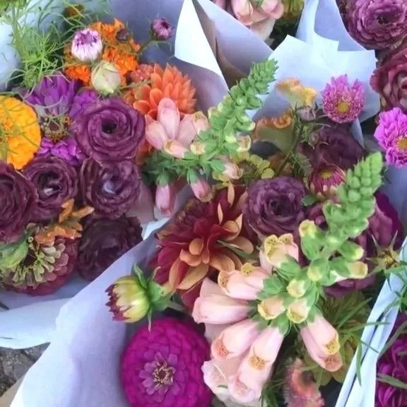 Various colorful flowers including purple, pink, orange, and yellow blooms arranged in bouquets with some wrapped in white paper.