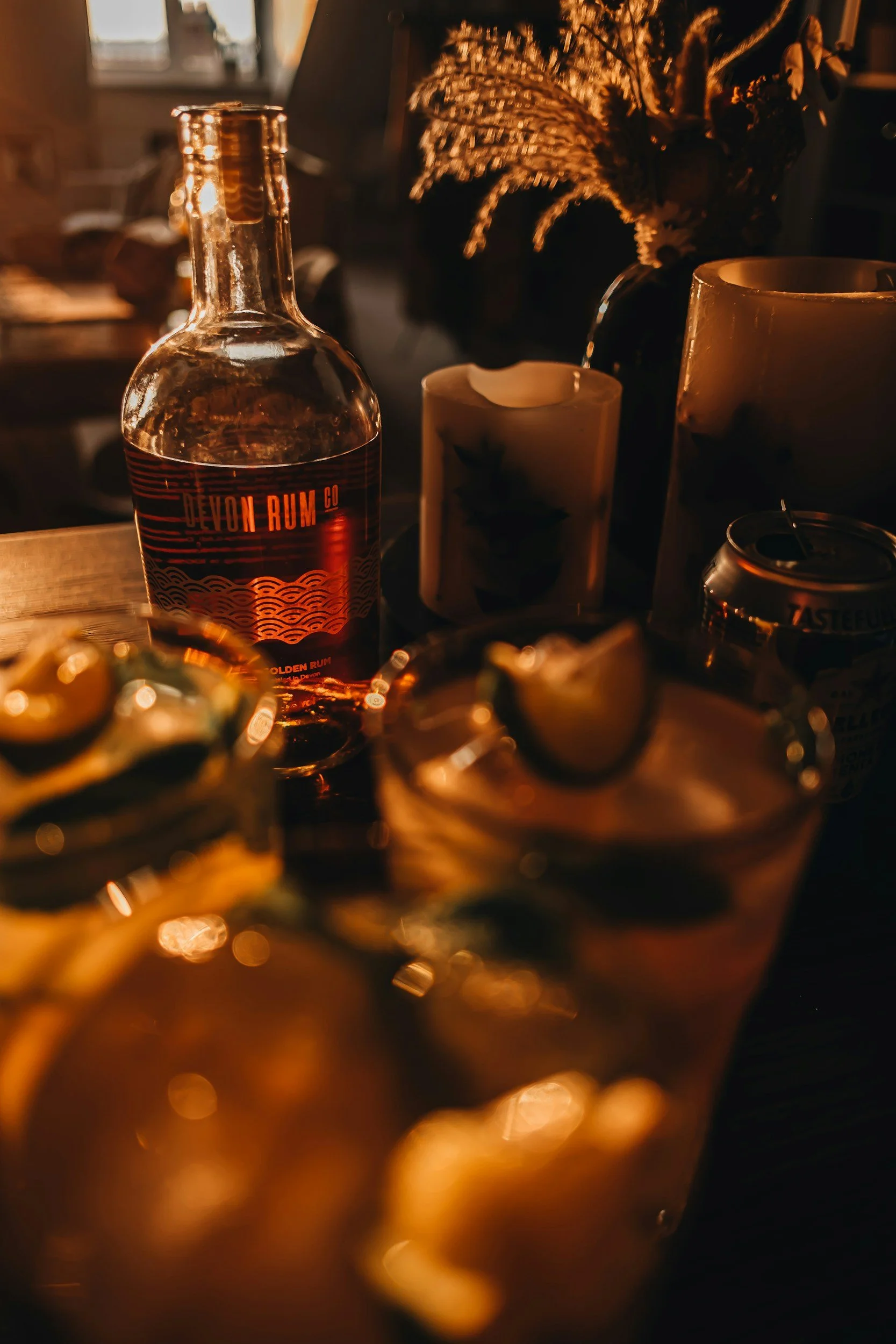 Dimly lit bar scene with a clear bottle of Devon Rum, candles, and glasses with lemon slices.