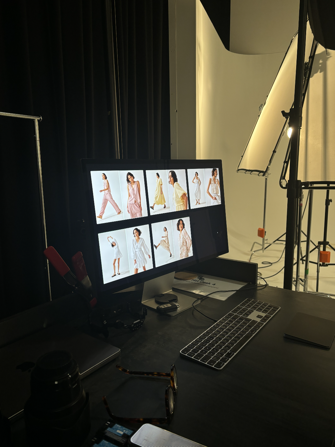 Photo of a photography studio workspace with a computer monitor displaying multiple fashion model images, studio lights, and a white backdrop.