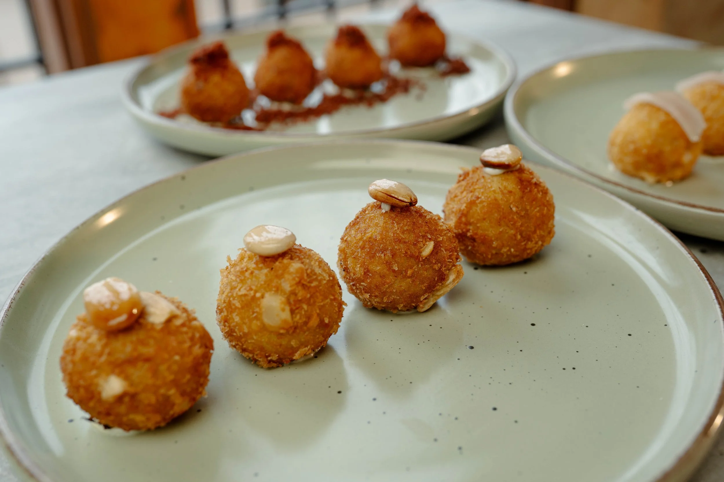 Croquetas de pollo a la pepitoria en un plato grande y otras en platos pequeños al fondo.