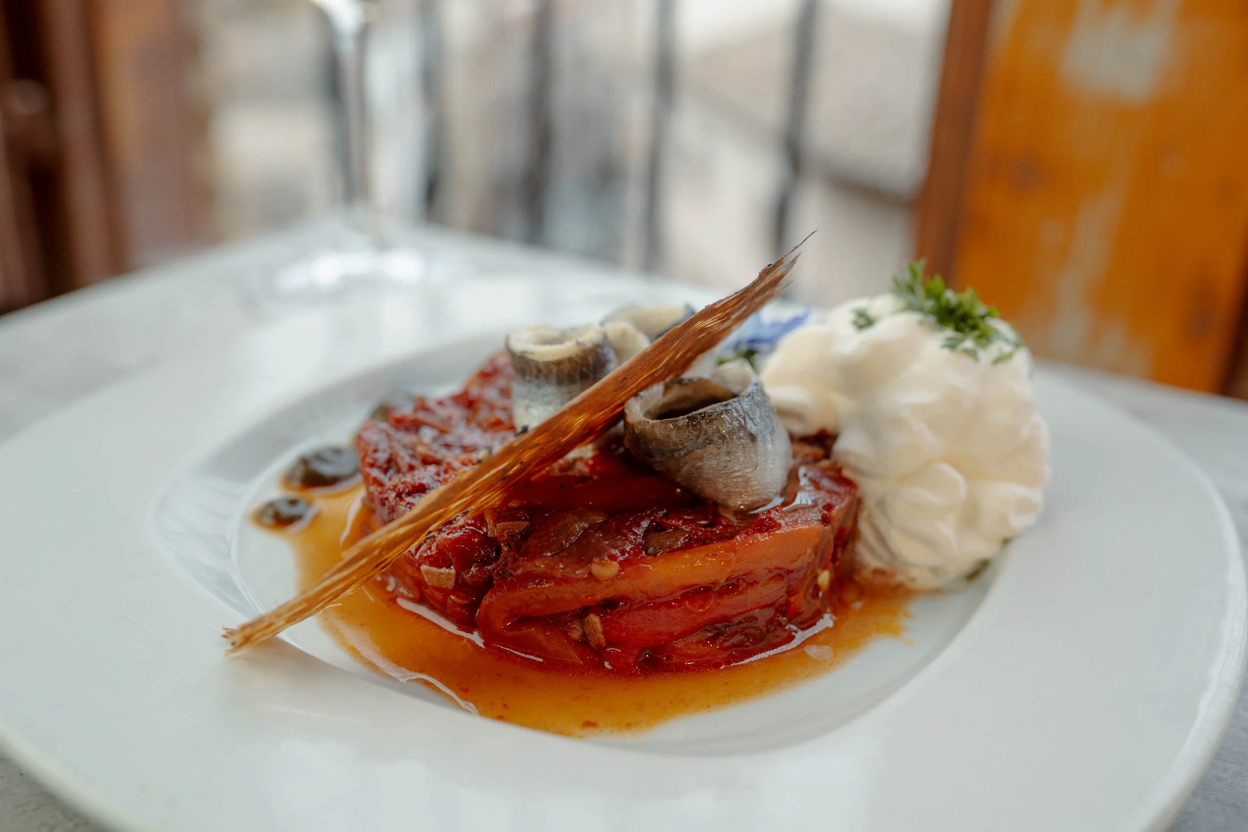 Plato de ensalada de asadillo manchego con chantilly de ajo blanco y barquillo aromatizado con tomillo emplatado frente a una ventana con vistas a Toledo

