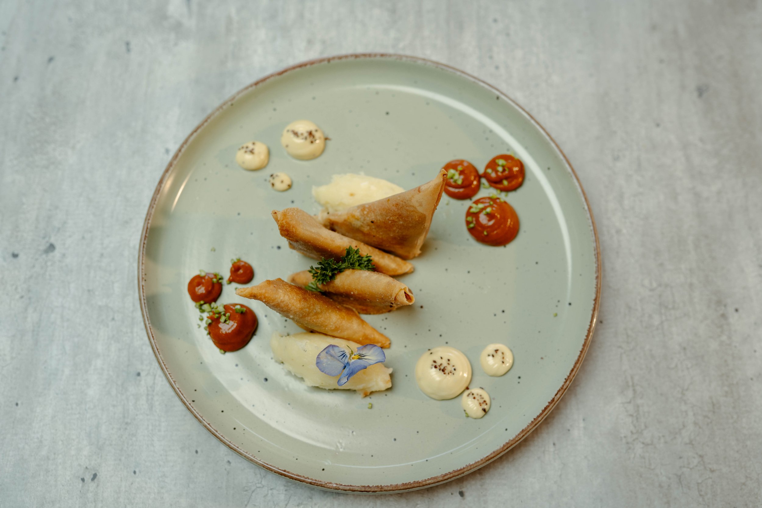 Plato de Samosas de pisto manchego con mayonesa de huevo frito, kétchup de chorizo y brandada de bacalao emplatado.