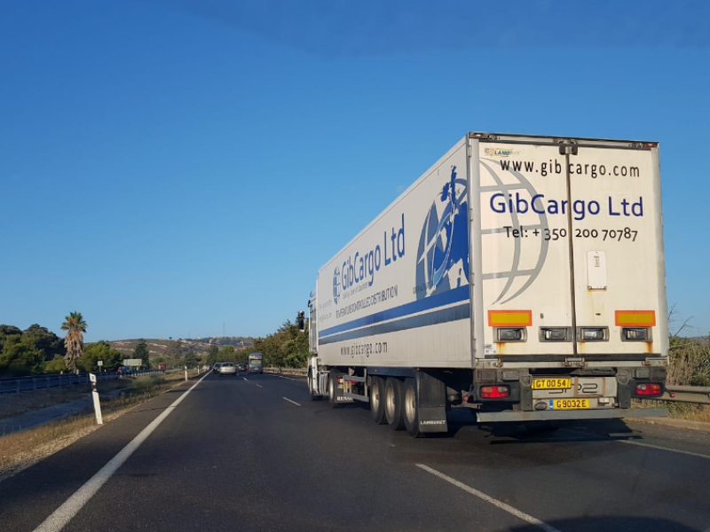 A white GIB Cargo Ltd truck driving on a highway with a blue sky, with trees and hills in the background.