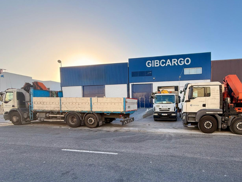 Three trucks parked in front of a blue and white GIBCARGO warehouse.