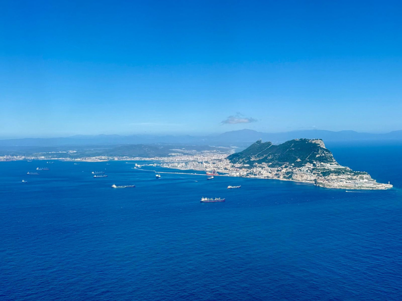 Aerial view of a coastal city with a mountain, ships in the water, and clear blue sky.