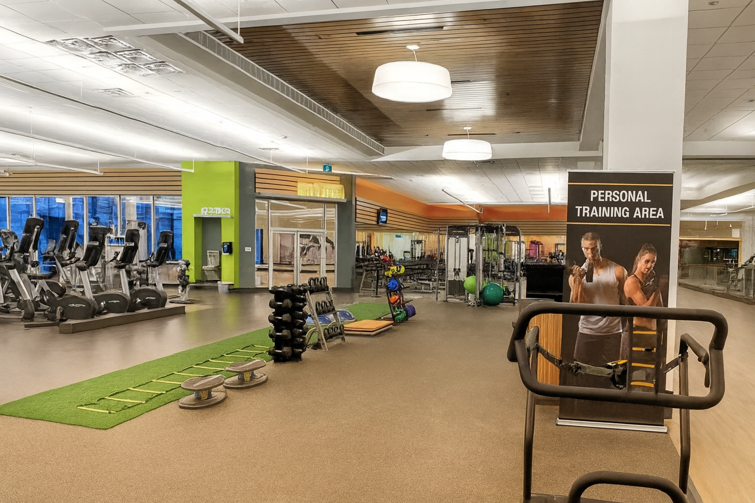 Empty gym with cardio equipment, weight racks, and a personal training area sign.