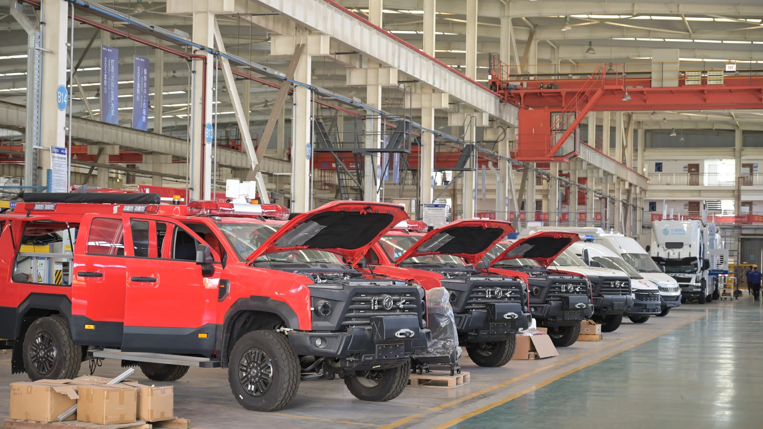 Factory with several red and white vehicles, some with open hoods, inside a large industrial building.