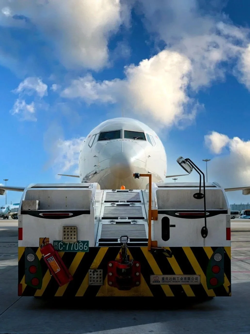 A large commercial airplane at an airport gate with a jet bridge, seen from the front, under blue sky with clouds.